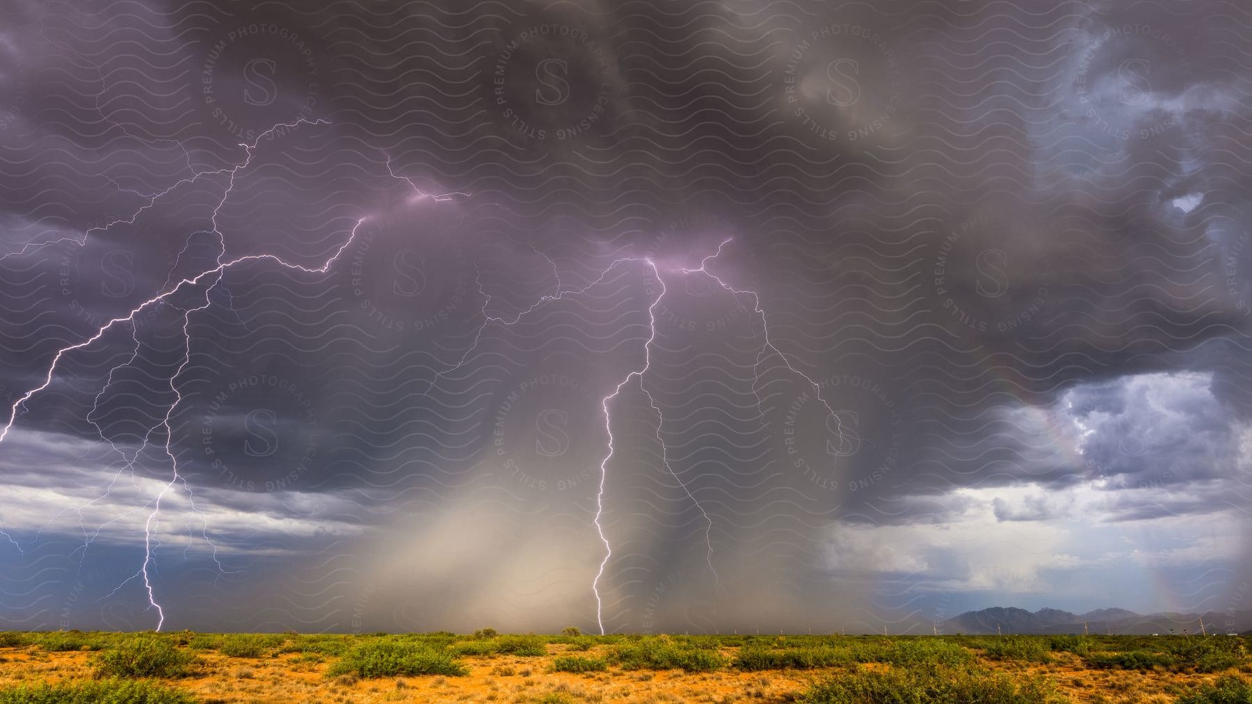 A dark cloud with lightning strikes over a sandy land with patches of green grass