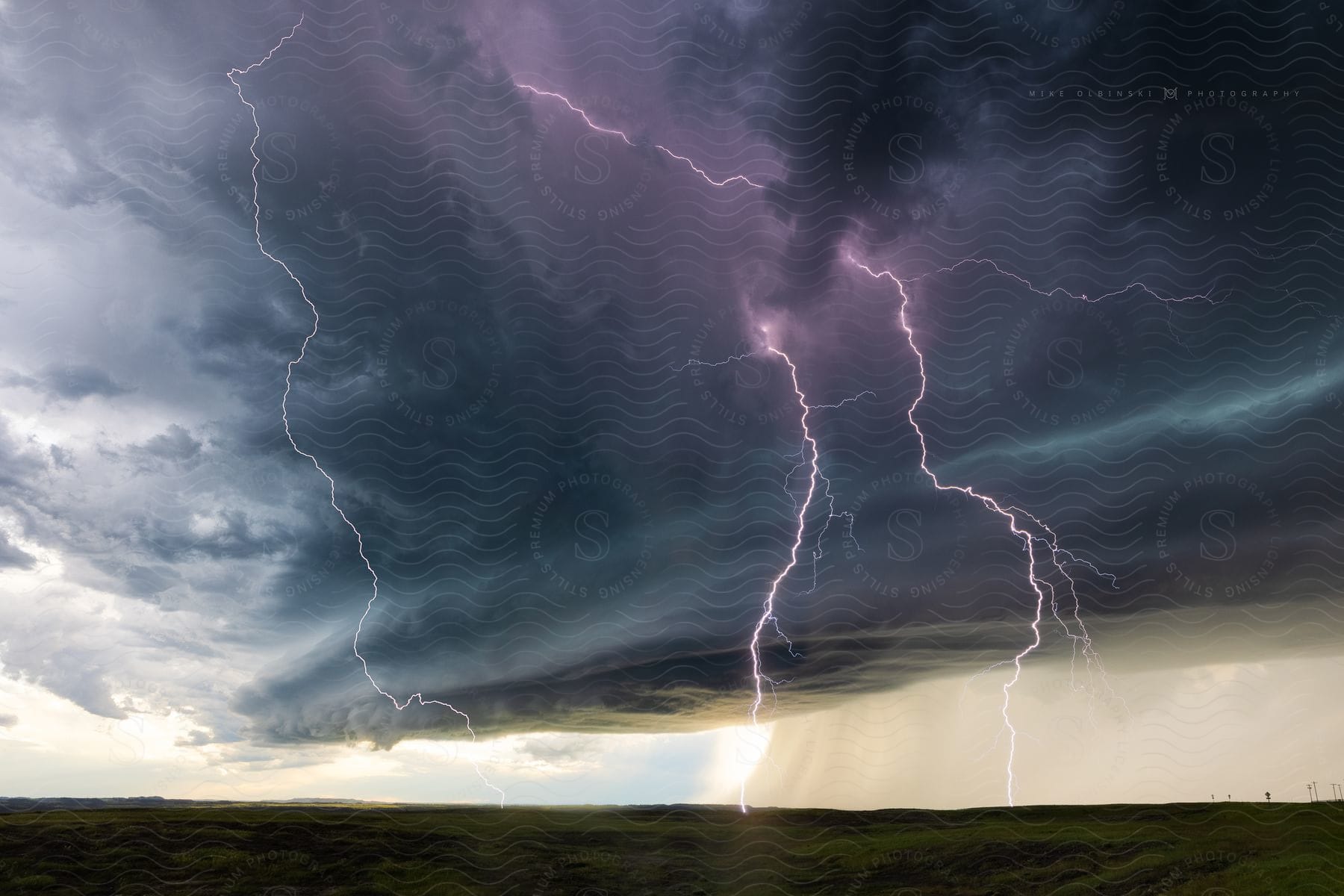 Stormy day with dark cloud crackling with lightning casting purple light across the sky as heavy rain pours down