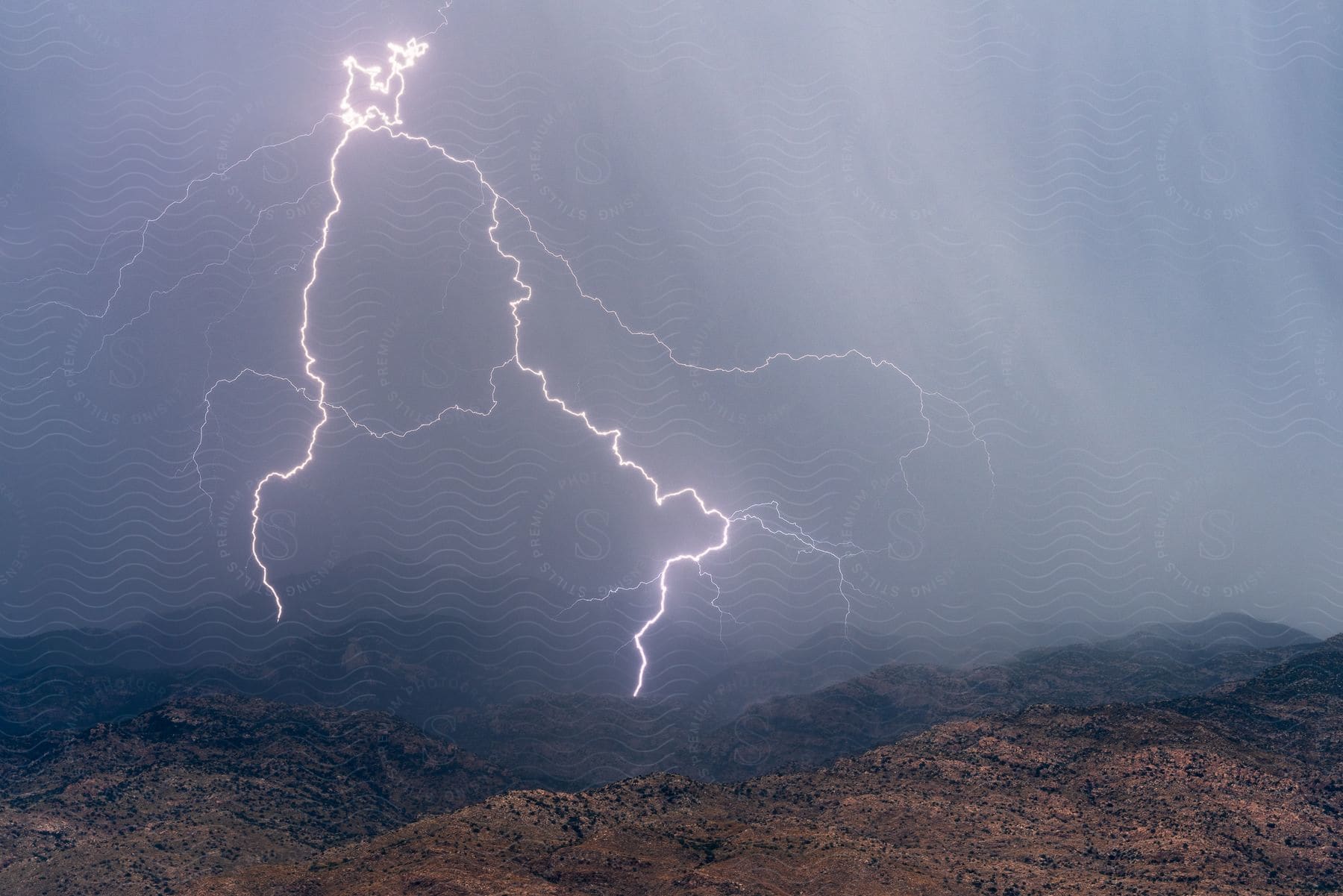 Large lightning bolts strike the hills of the rincon mountains under a dark cloudy sky