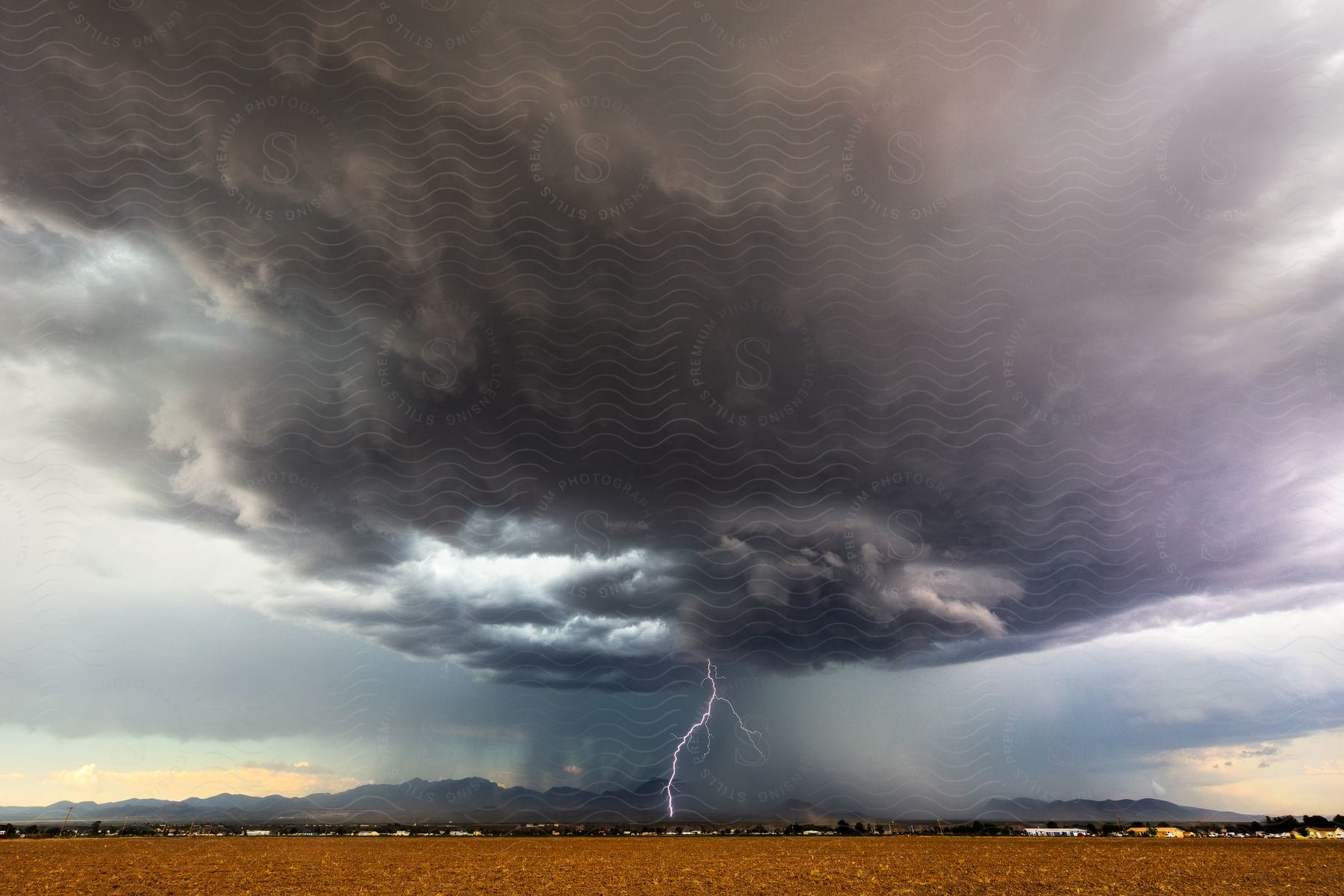 Lightning strikes from a storm cloud over a rural community with mountains in the distance