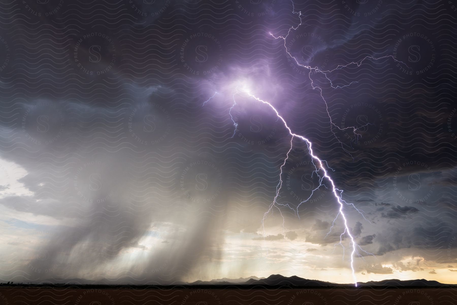 Lightning and rain falling from storm clouds over the mountains in the plains