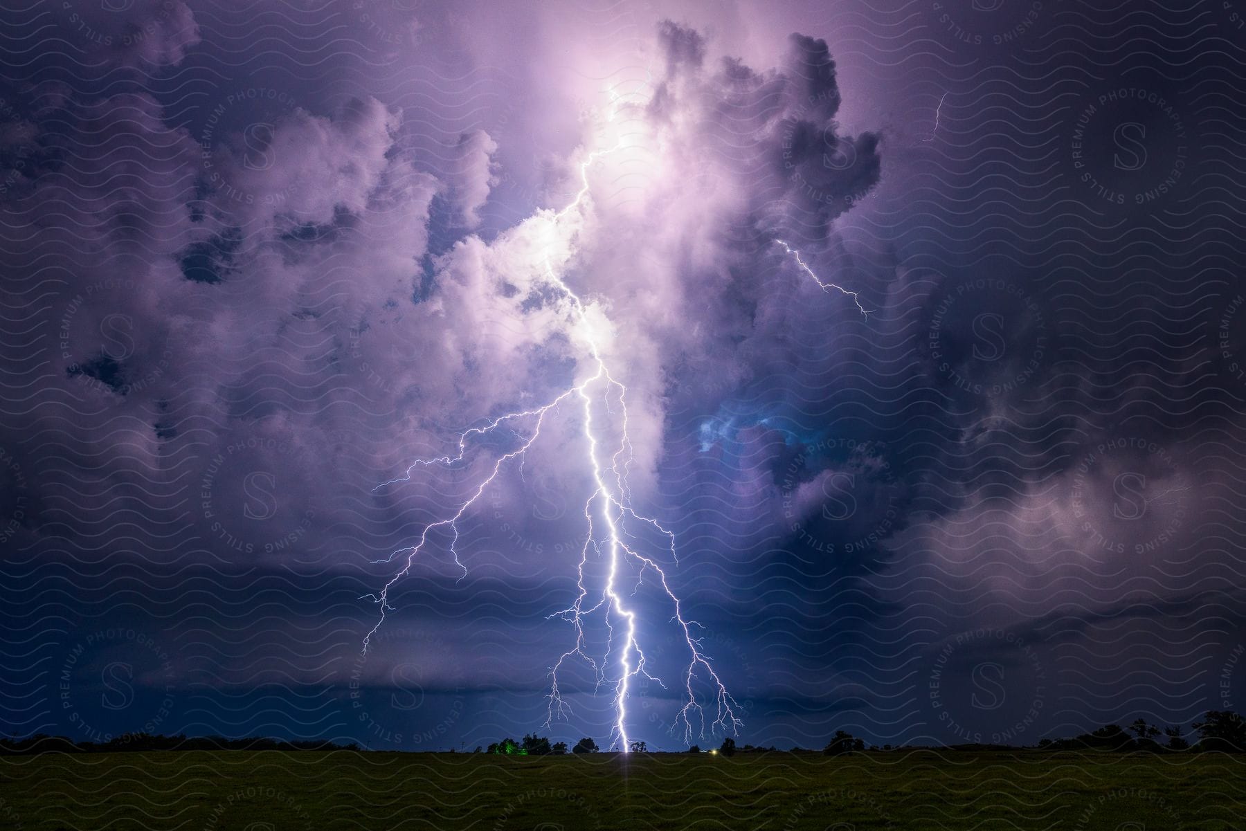 Lightning strikes in the distance of a grass flatland field lighting up a cloudy sky at night