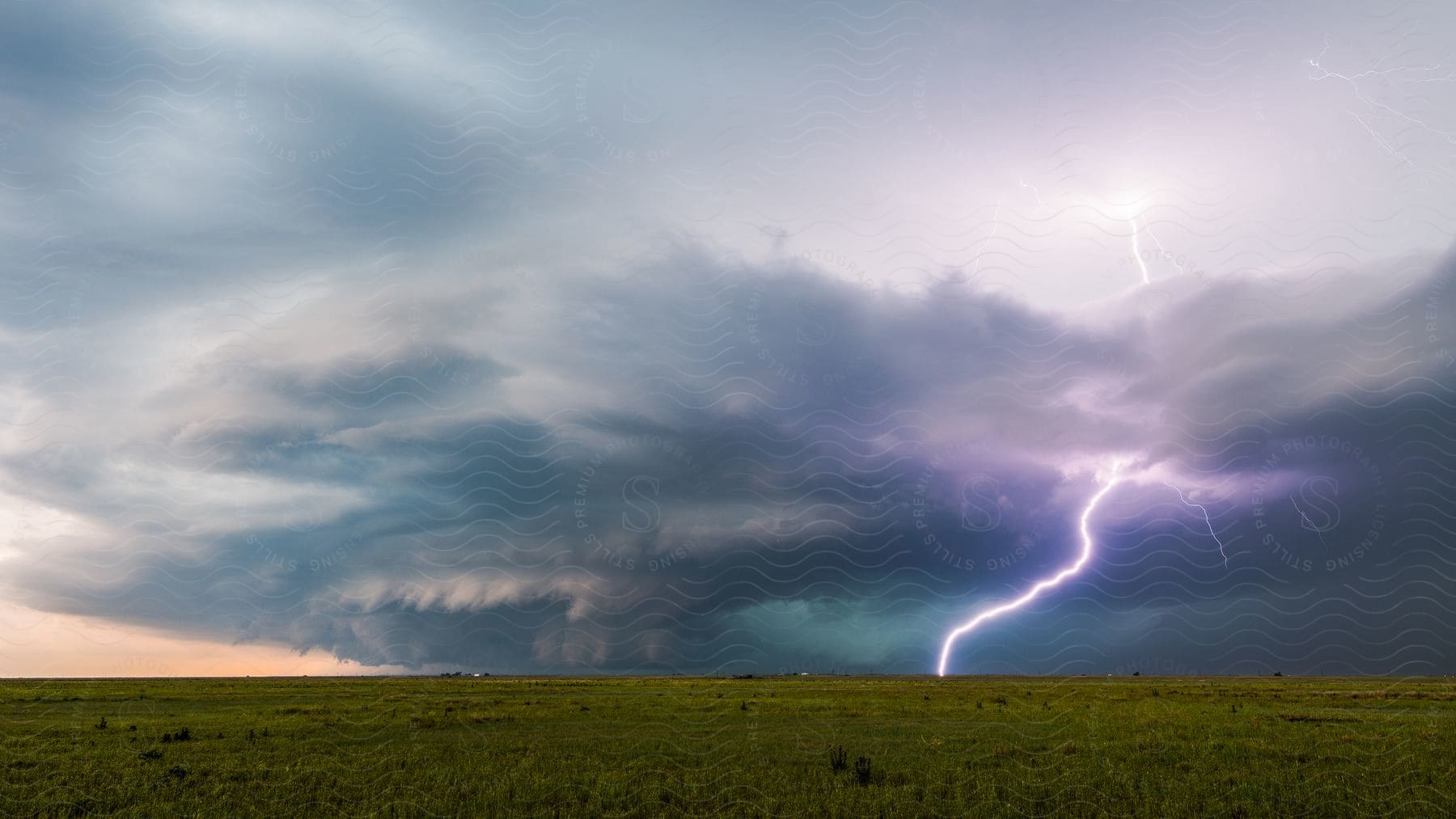 A bright lightning bolt strikes the ground as a storm supercell moves over rural land