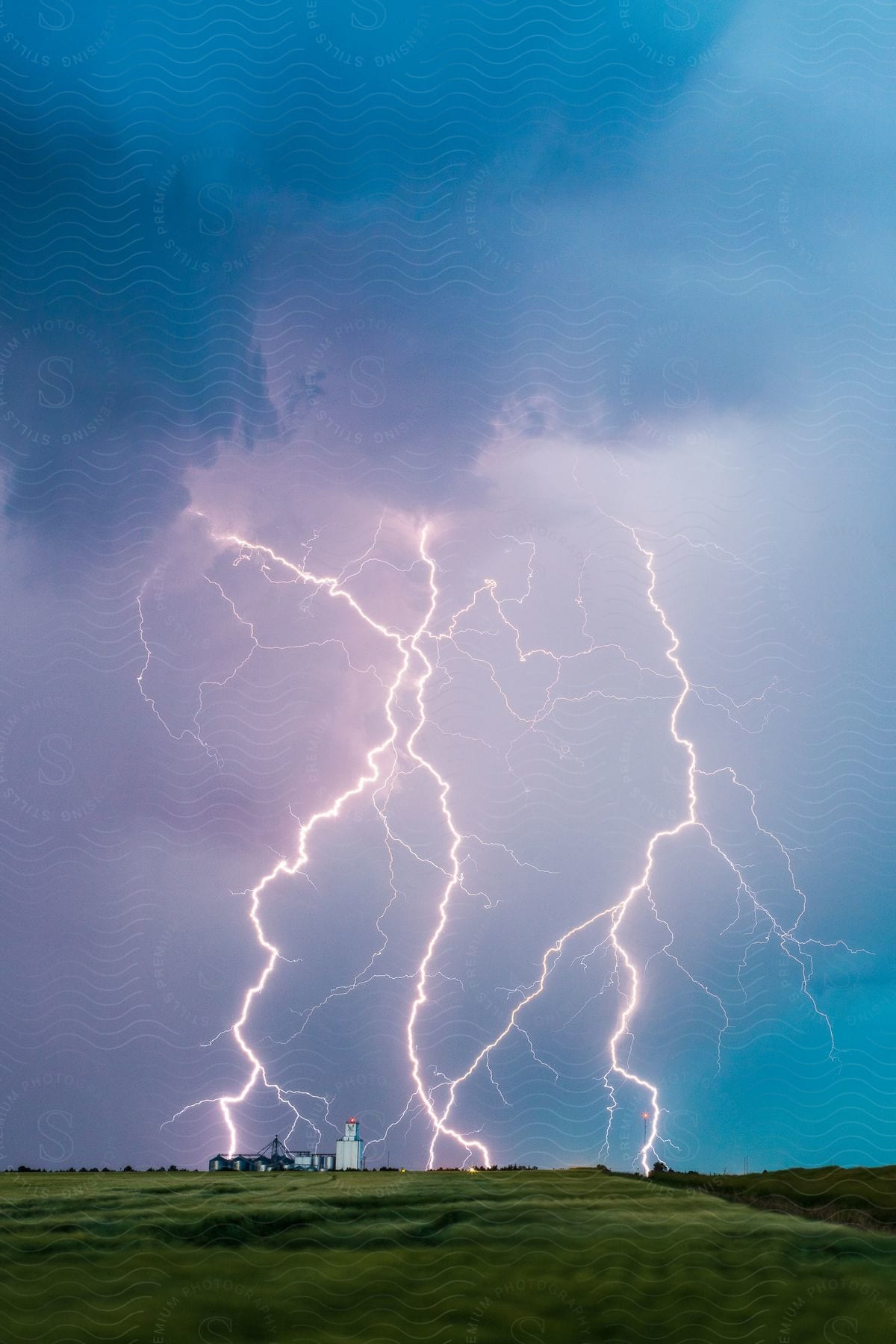 Multiple exposure shot of lightning strikes on a field near silos during the daytime