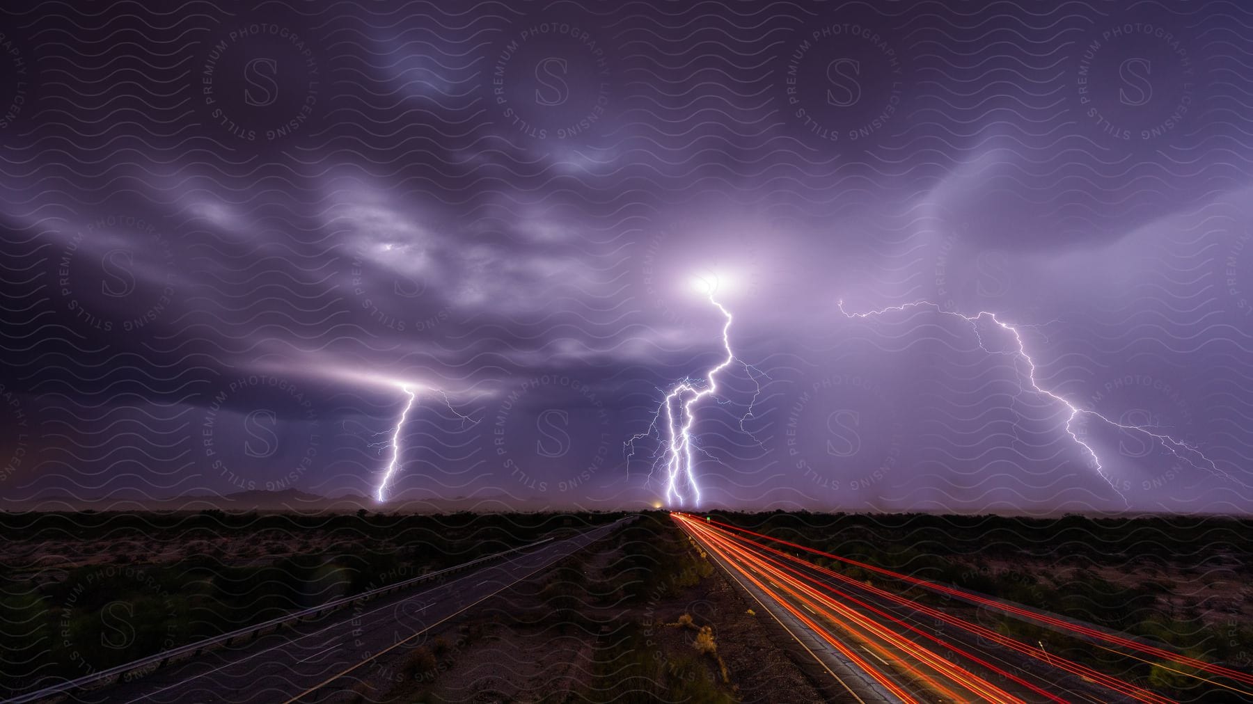 Lightning storm illuminates desert wasteland as cars dodge bolts in distance motion from car lights illuminates dark road