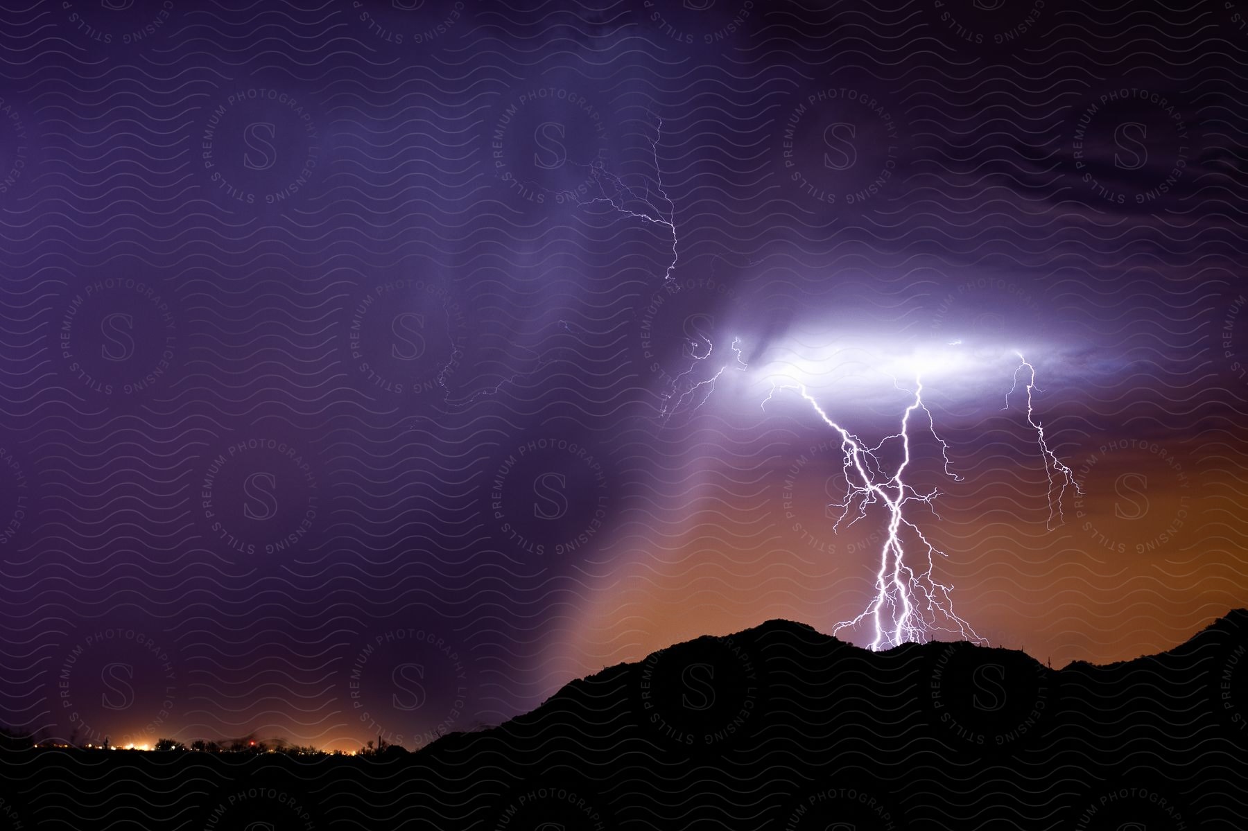 Lightning strikes over mountains as rain falls on a small town