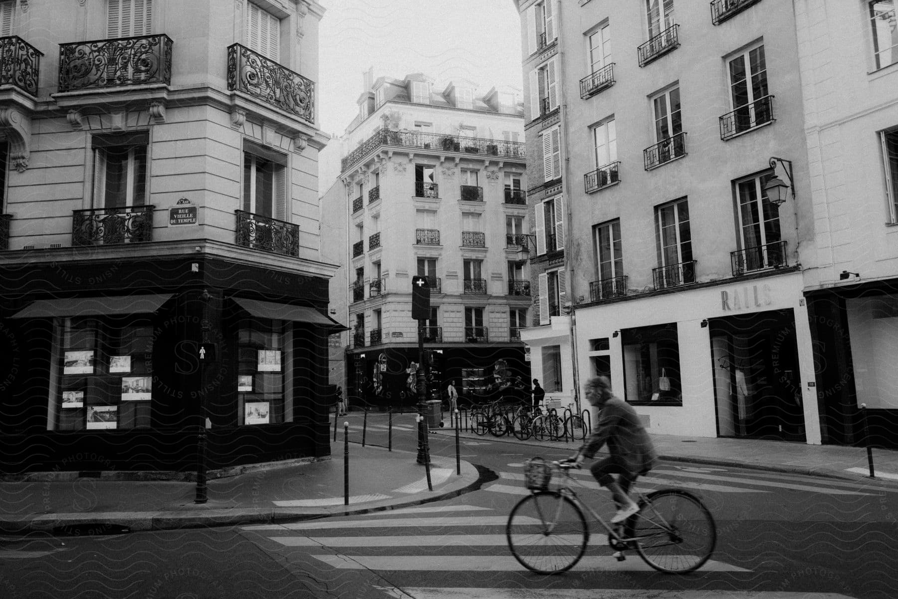 A man is riding his bicycle through a city street surrounded by buildings