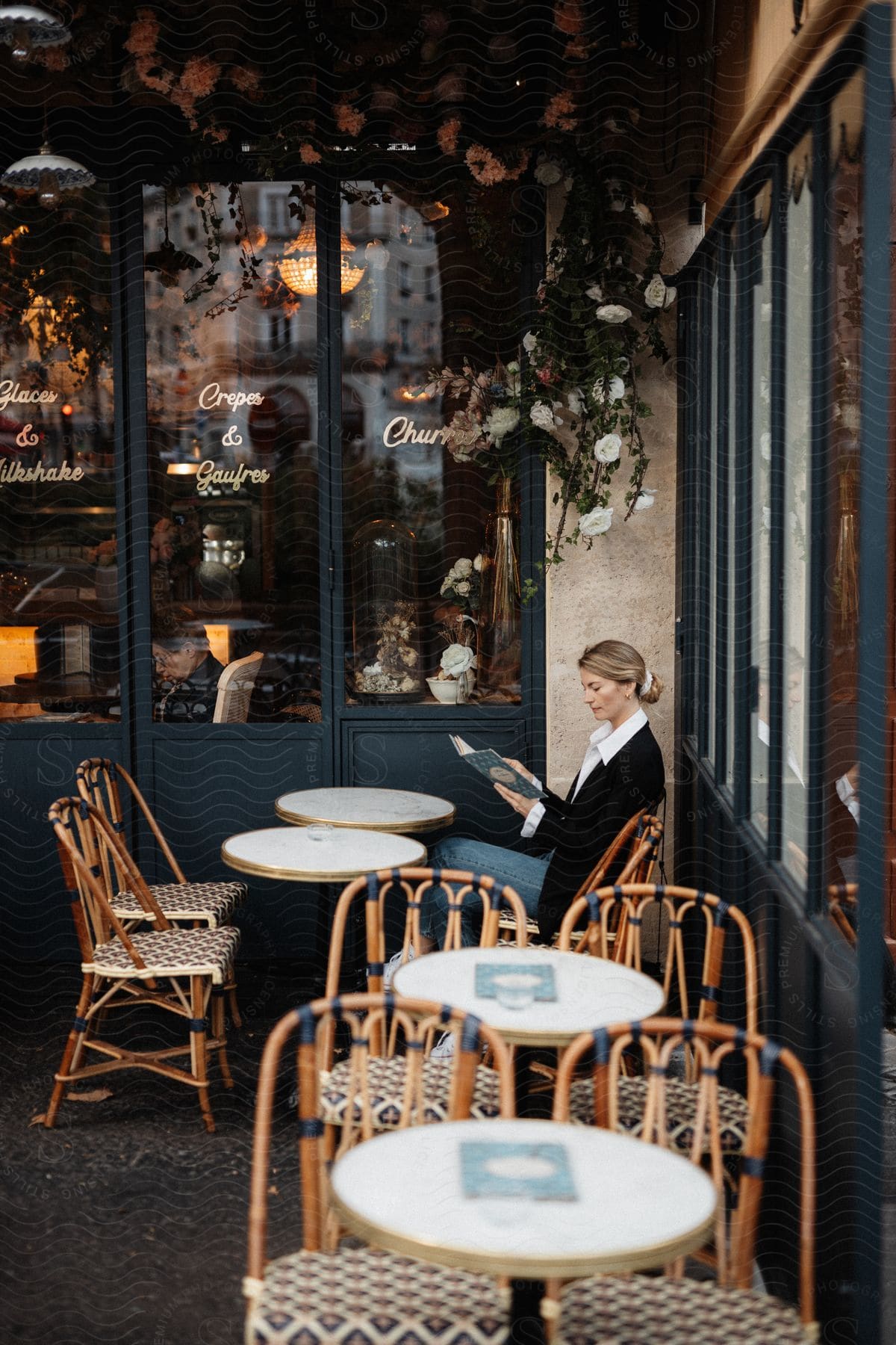 A woman sitting at a cafe table outdoors reading a book