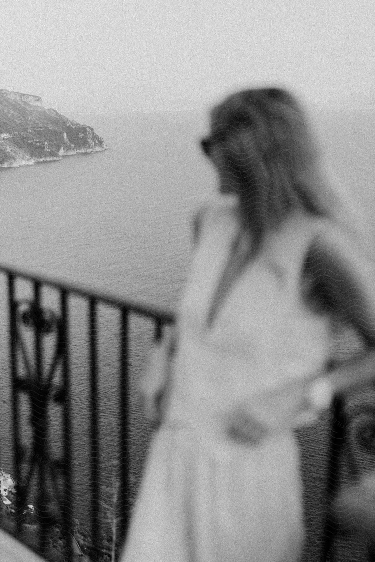 Woman leans back and elbows on railing turning her head to look at the ocean and rocky shoreline