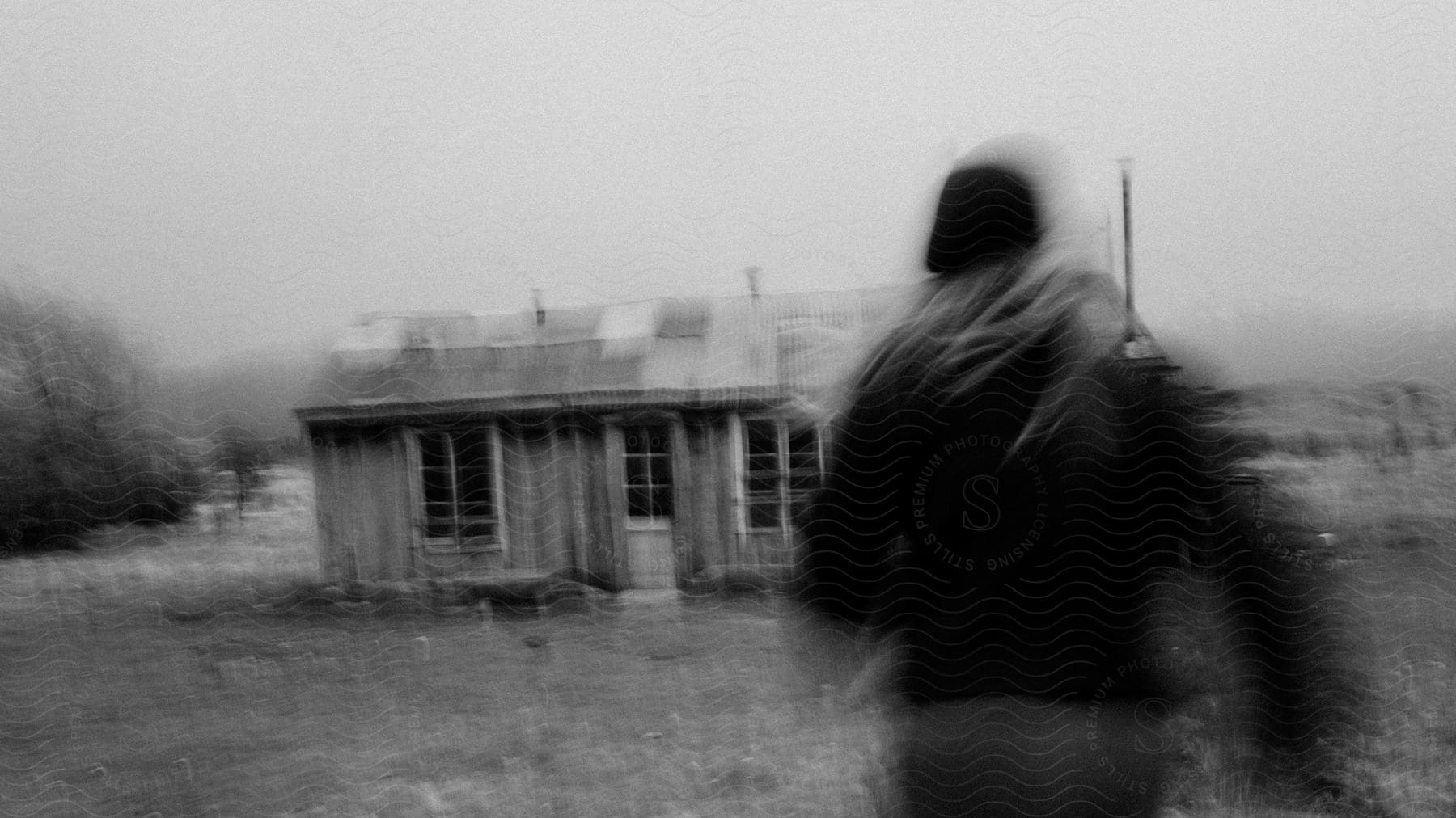 A black and white photograph of a woman running towards a building in a rural area