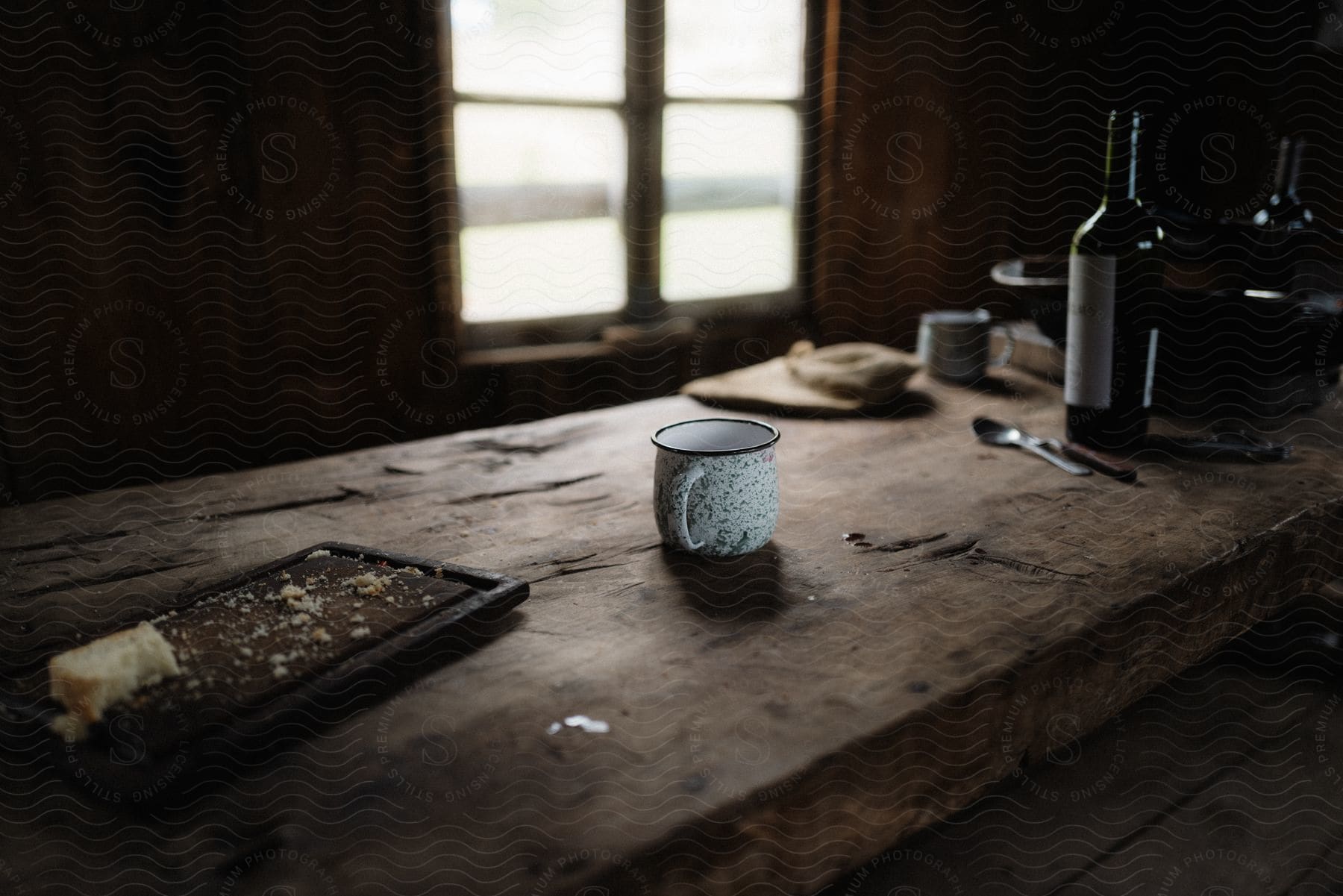 A wooden table with a cup and bottle on top near a window