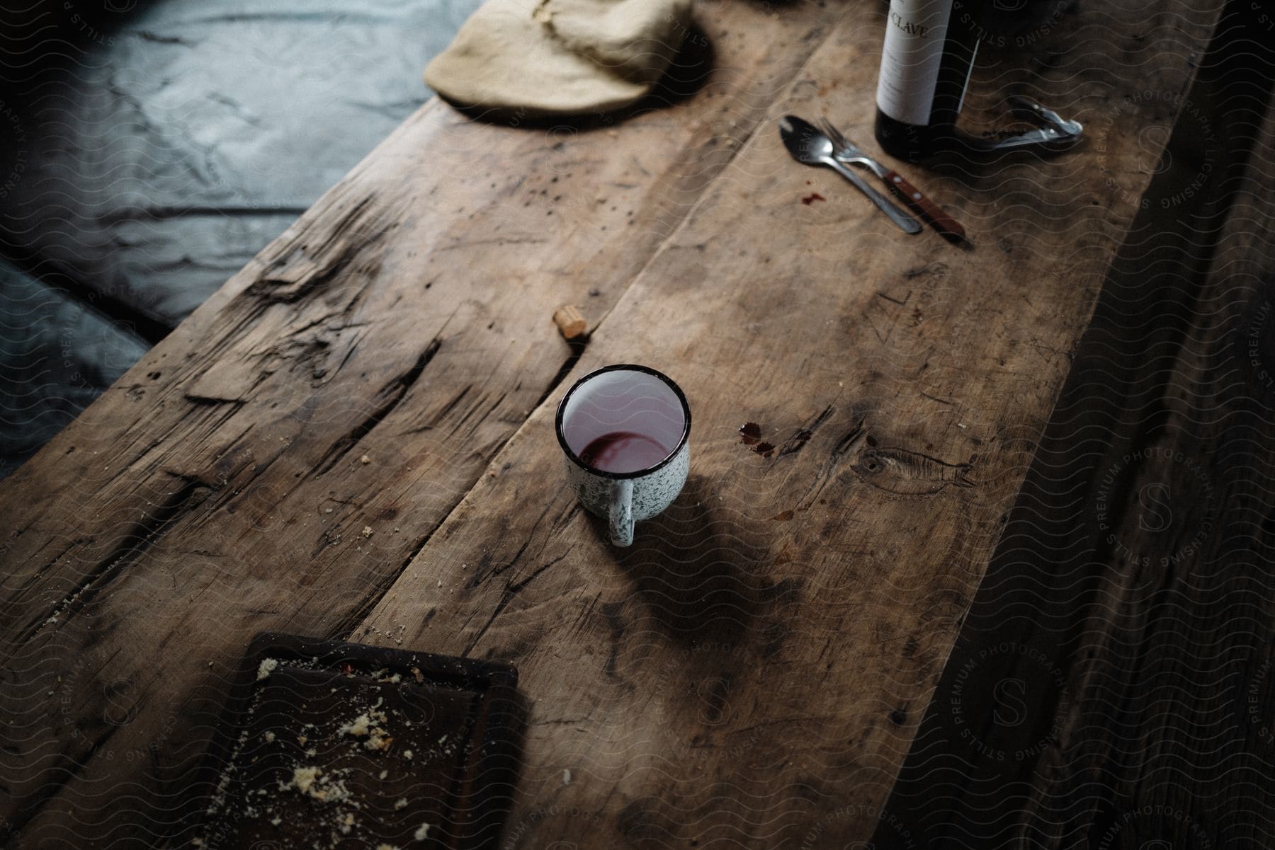 Remnants of a meal on a rough wood table including a wine bottle silverware crumbfilled tray and coffee mug