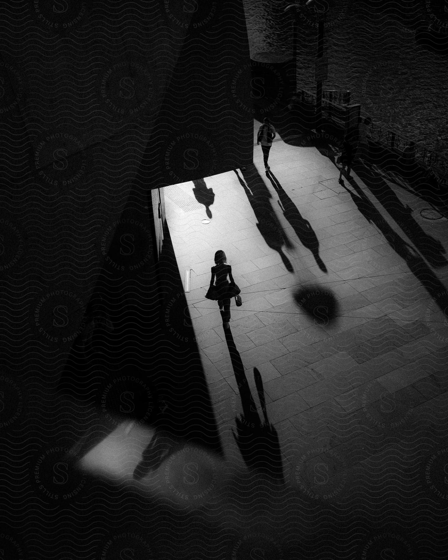 Pedestrians walking near a pier with only their shadows and silhouettes visible