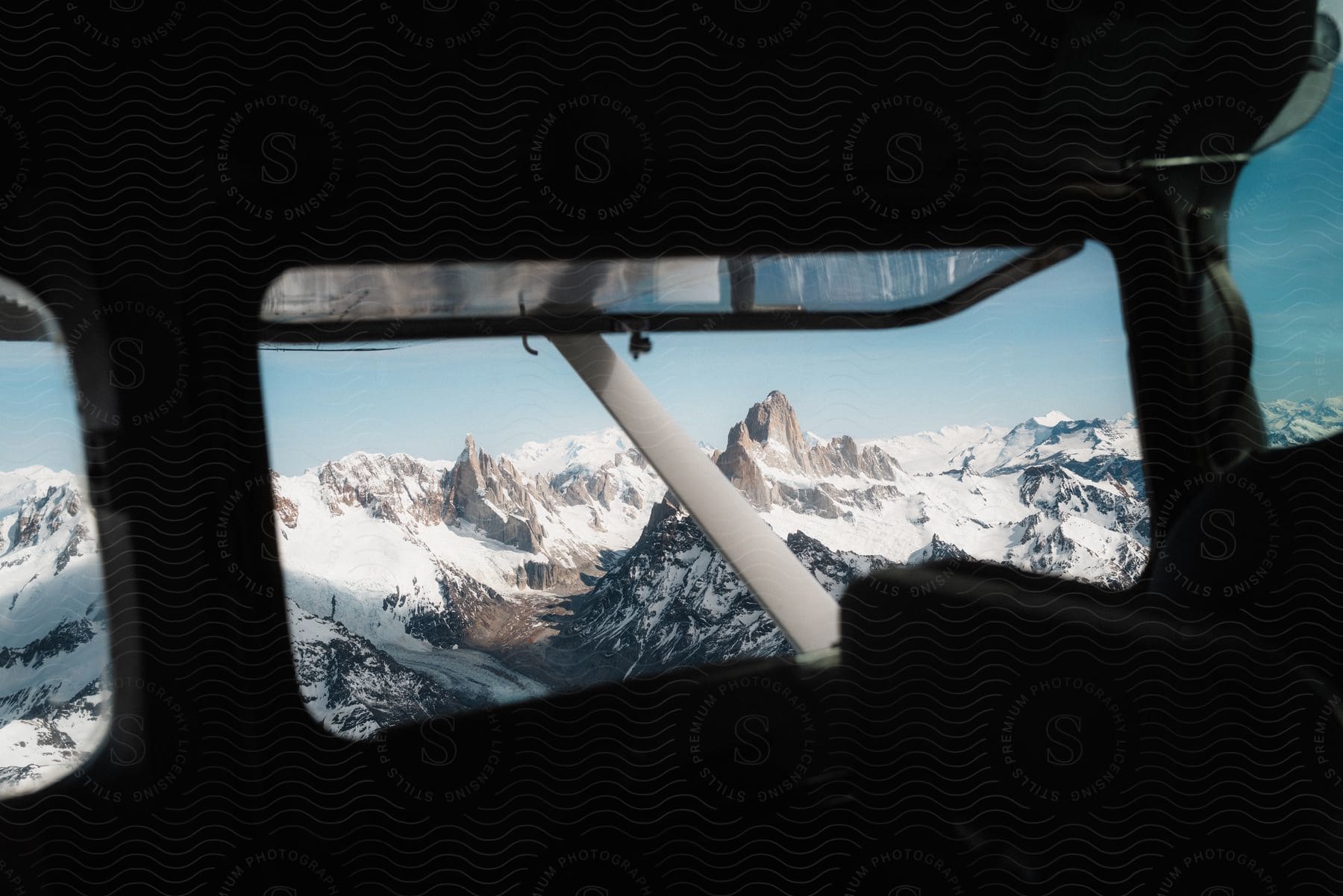 A snowy mountain range seen through the window of a small airplane