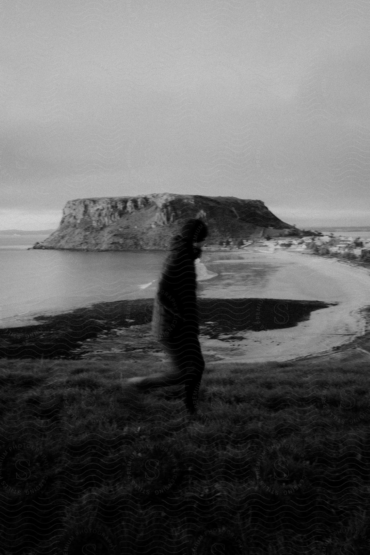 A black and white image of a man walking alone near a beach with a mountain in the water