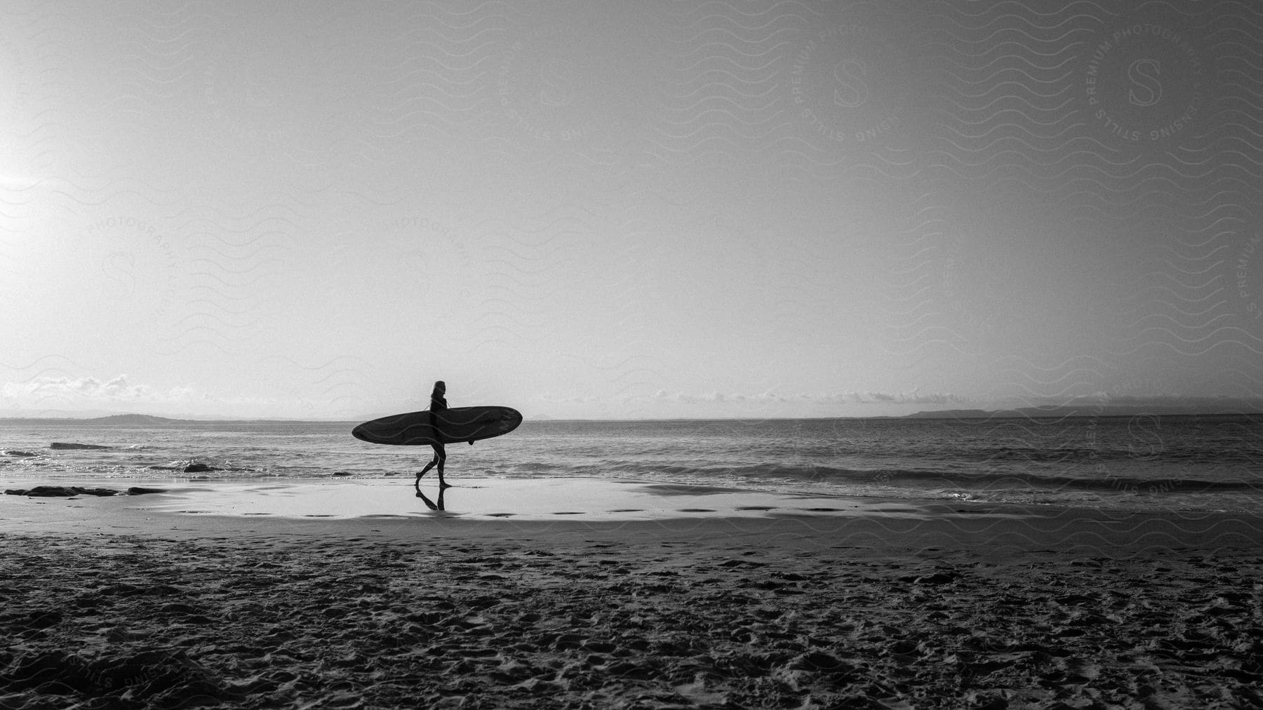 Silhouette of a woman carrying her surfboard across the beach