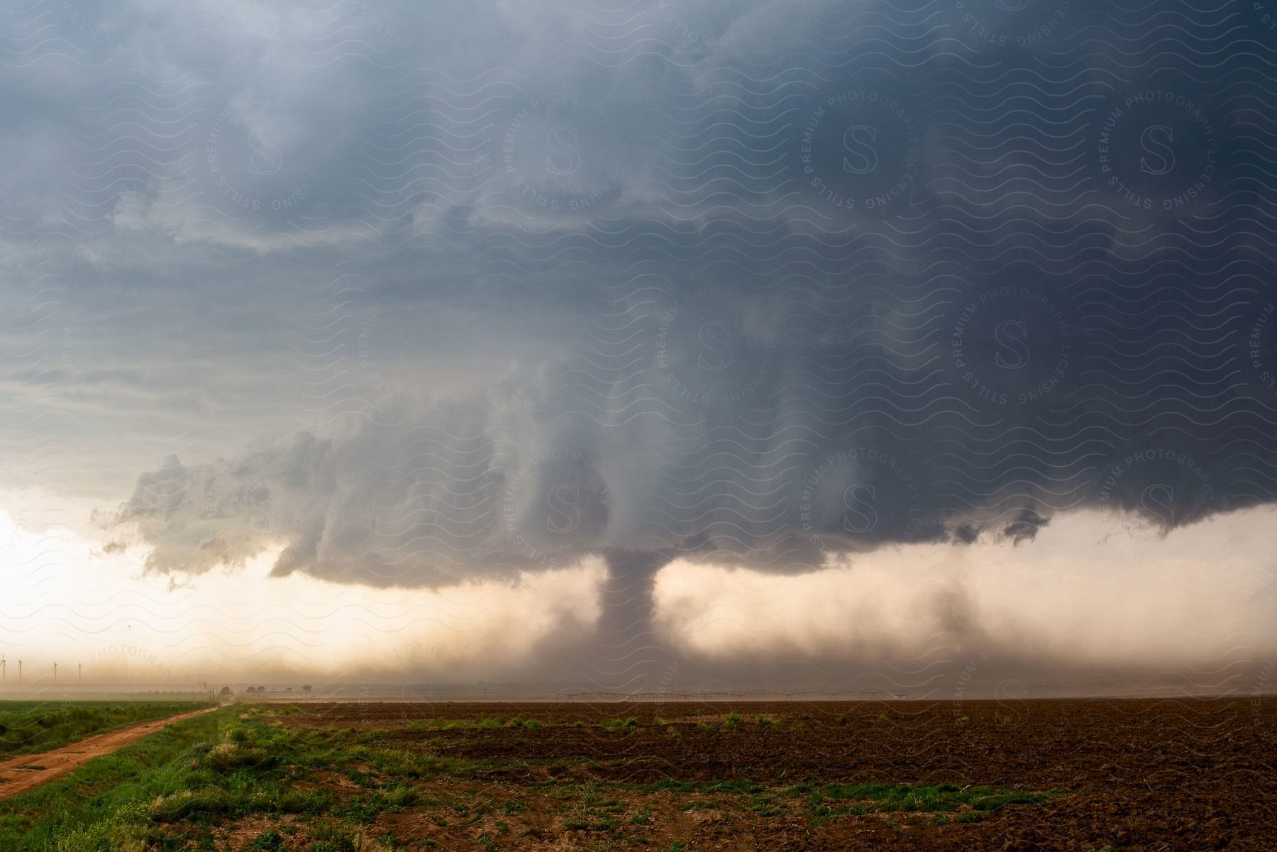 A funnel cloud is seen on the ground near a rural road as a storm moves over farmland