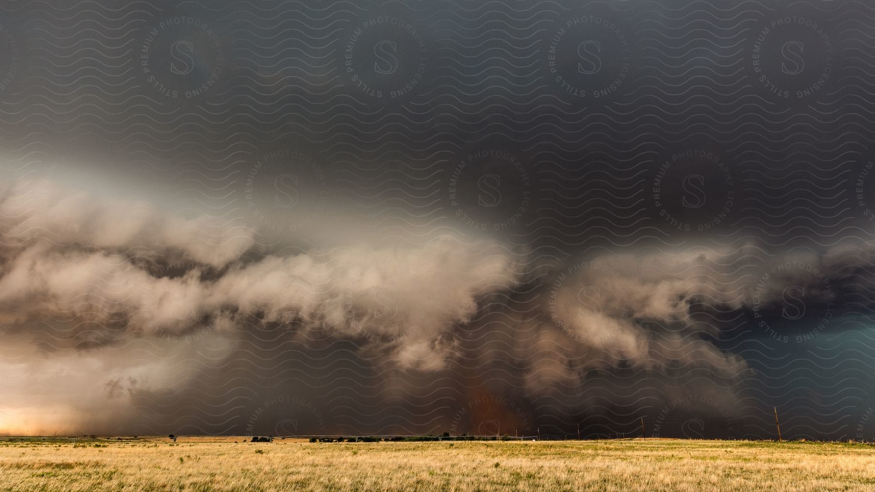 A dark supercell storm cloud pours down rain as it moves over rural land