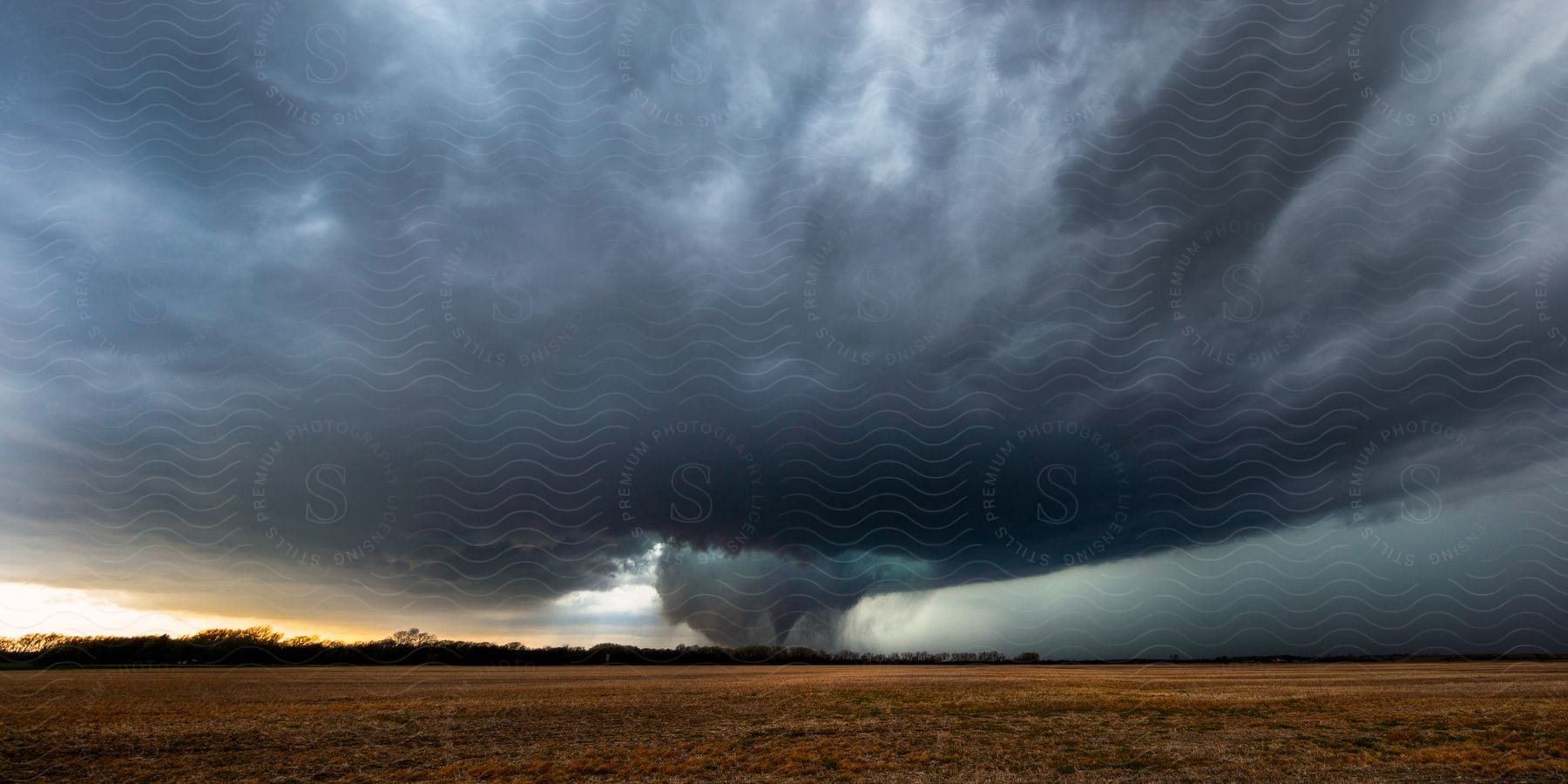 Dark storm clouds above a plain with a tornado forming at the center
