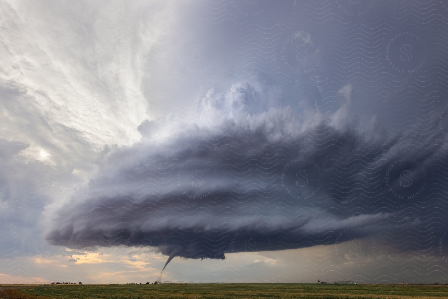 A funnel cloud emerges from a supercell storm cloud over an open field