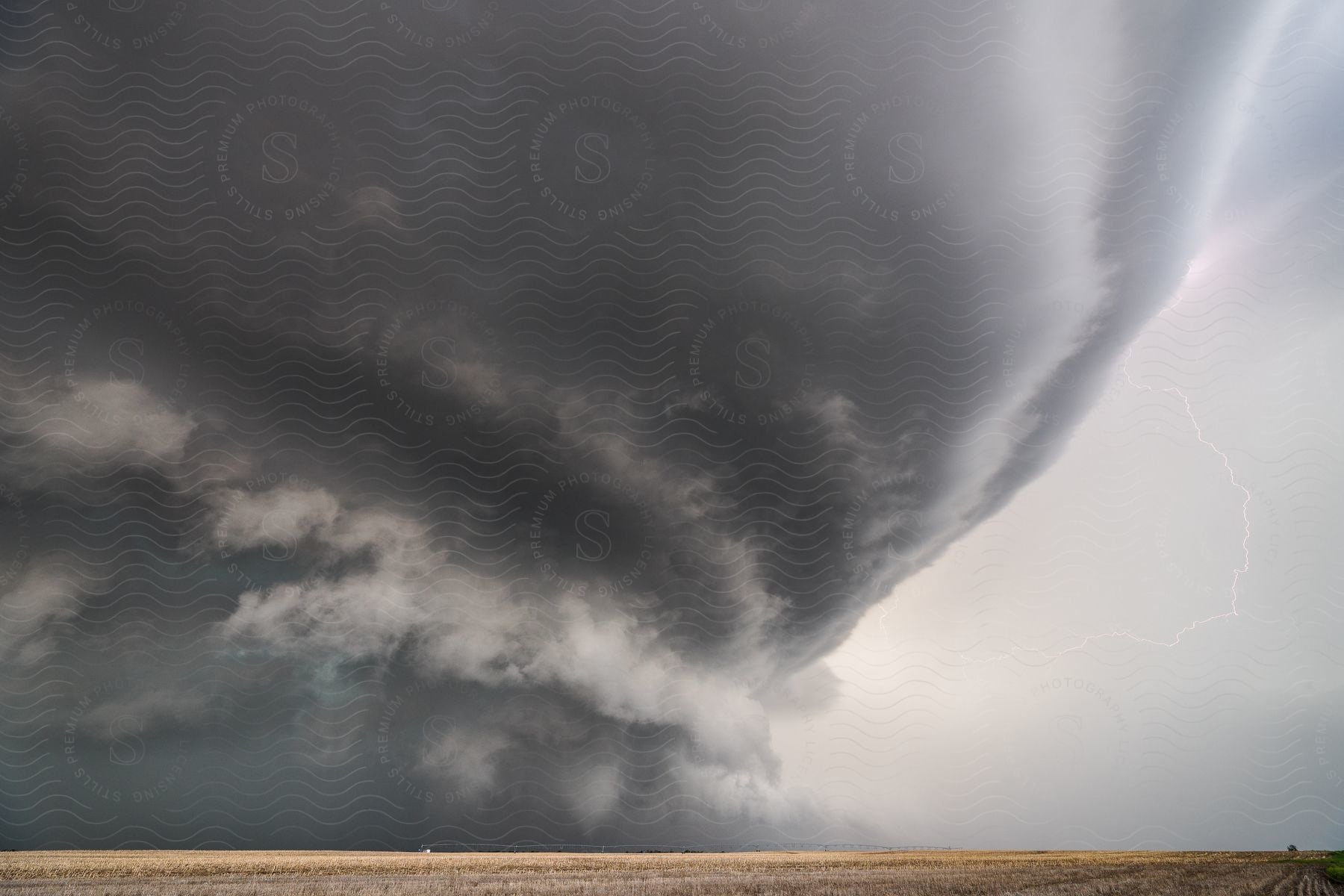 A dark supercell storm moves over rural farmland with lightning in the air