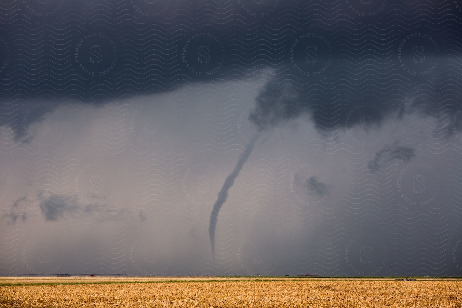 A twister moves over rural farmland as dark storm clouds cover the sky in felt texas