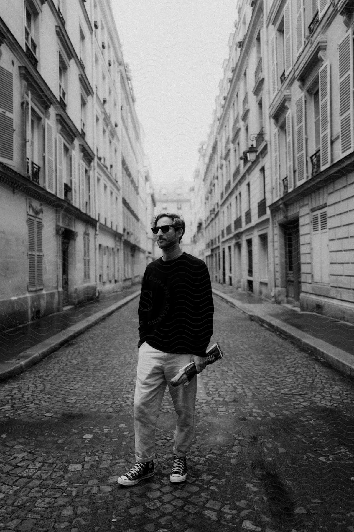 A man holding a baguette stands in the middle of a city street