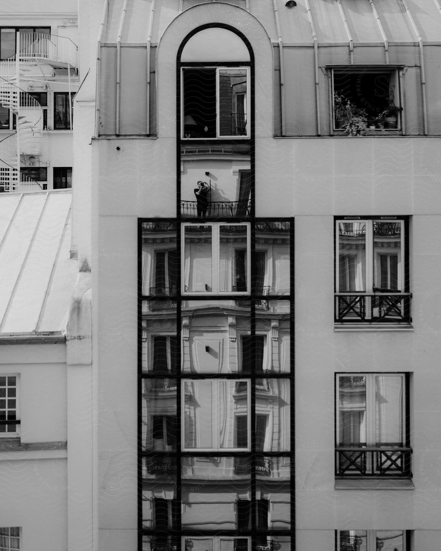 A black and white image of a person standing in front of a tall building taking pictures with a camera