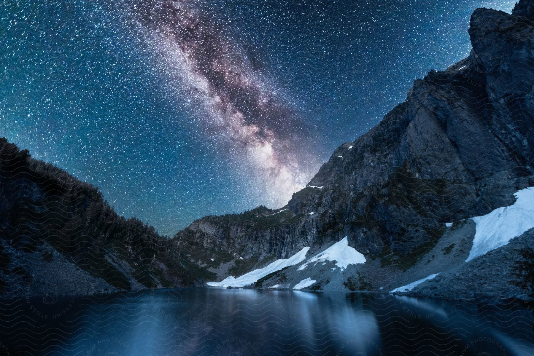 The milky way shines above a forested mountain river valley at night