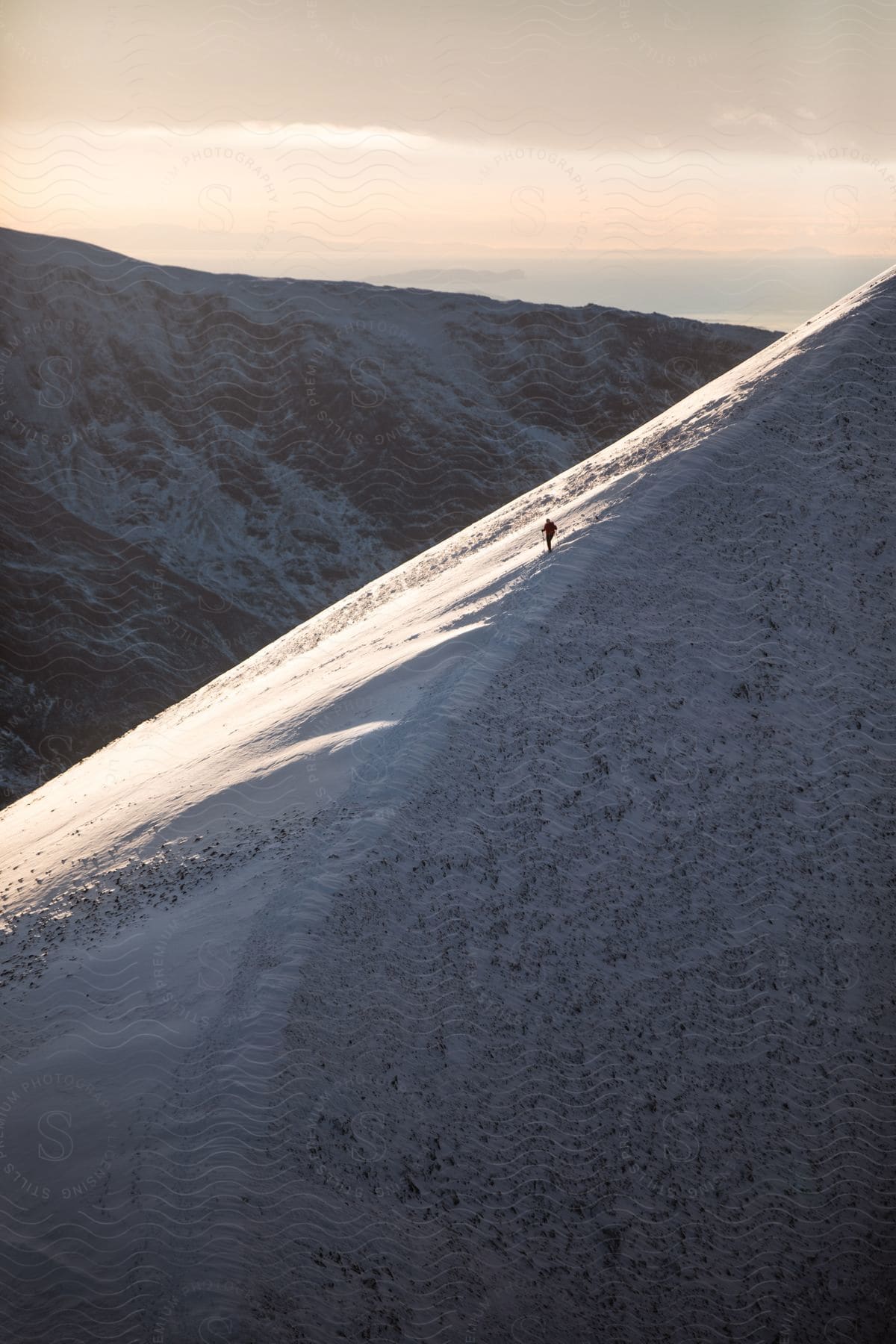 Mountaineer standing on snowcovered slope of mountain looking at sunset