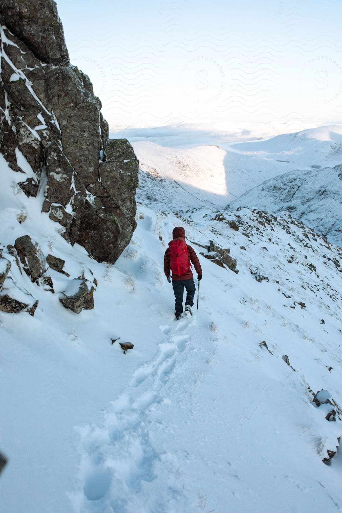 A man hikes across a snowy mountainside with mountains in the distance