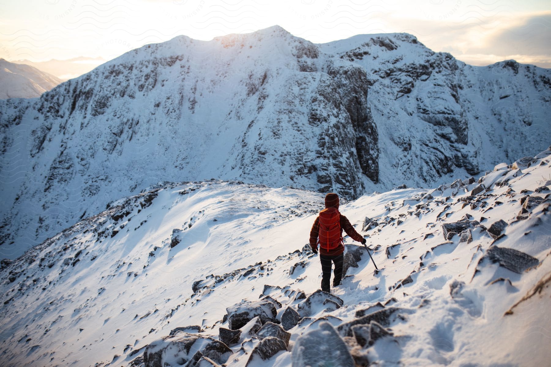 A young boy with a red backpack walking towards a snowy mountain