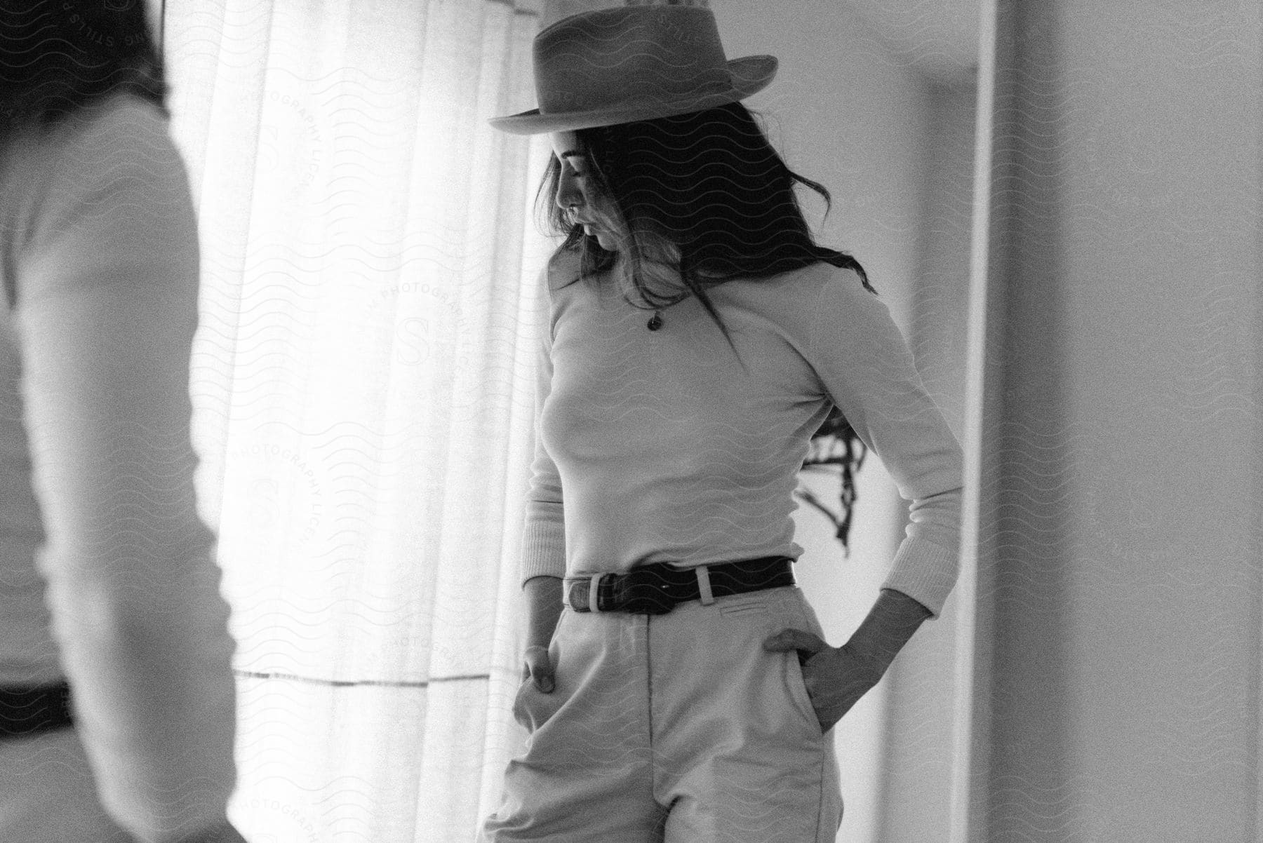 A woman models pants with a belt a longsleeved shirt and hat in a mirror