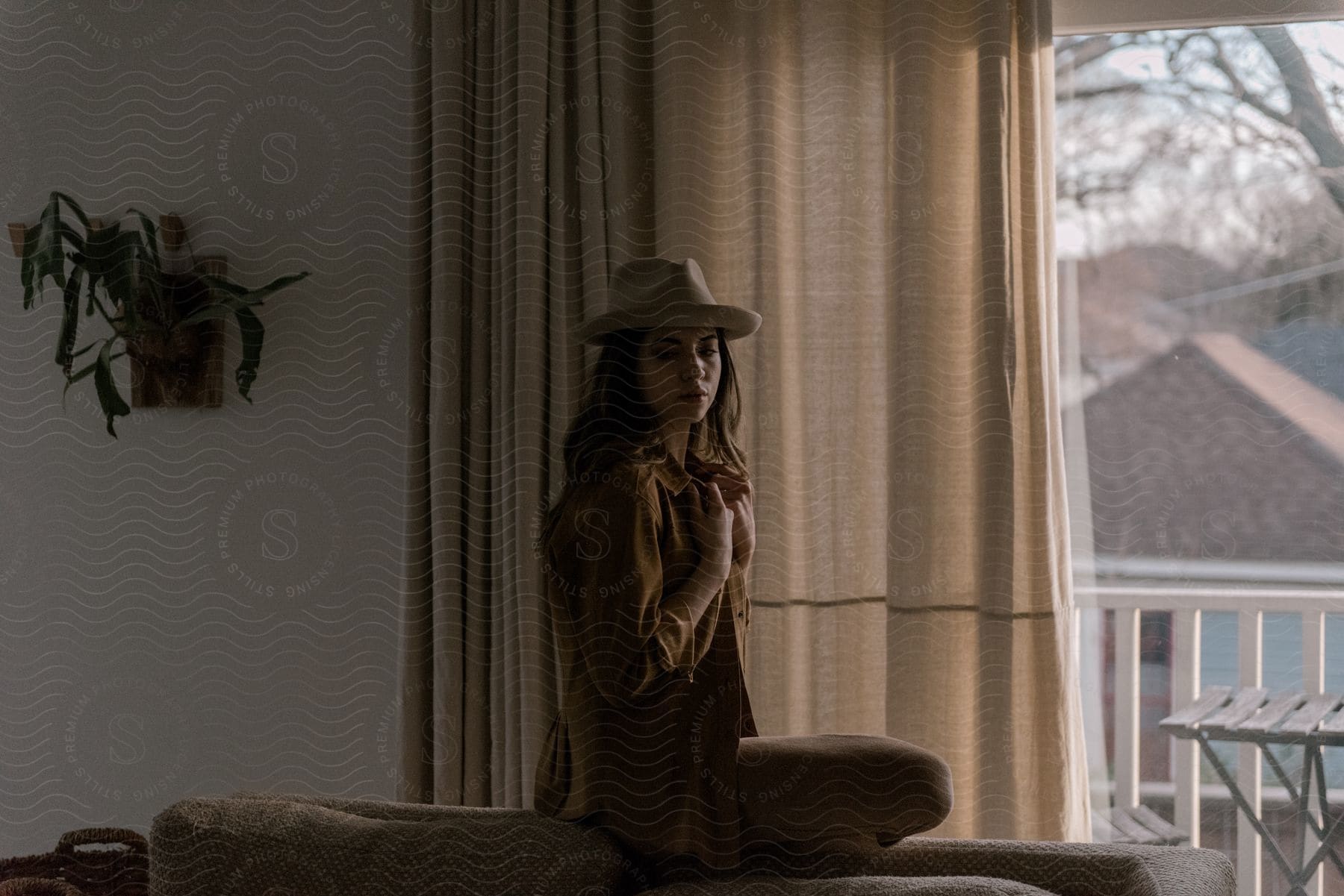 A woman standing near a window wearing a hat