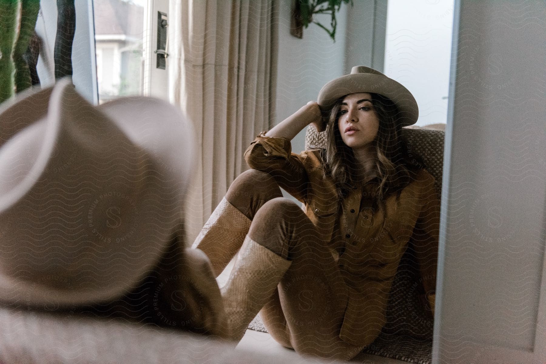 A person sitting in a southern apartment wearing a cowboy hat and fashionable clothing