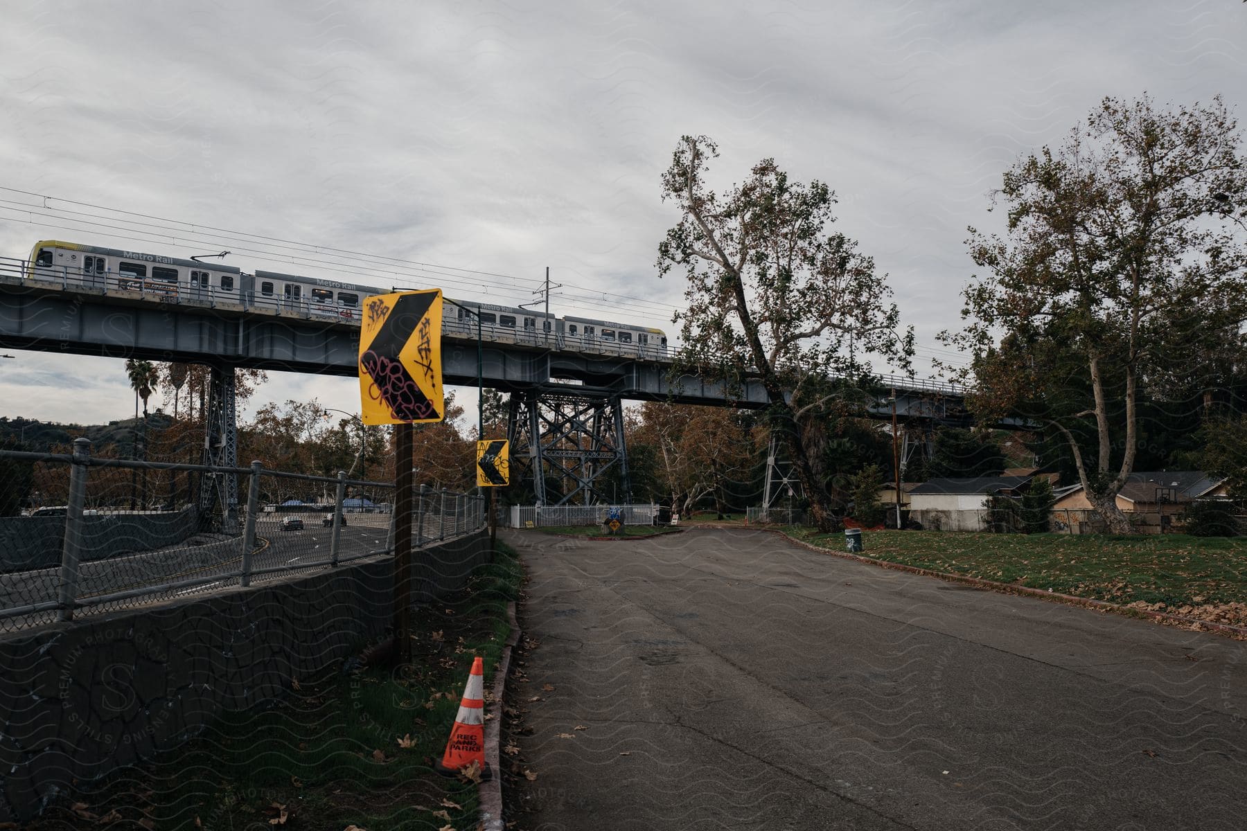 A community with a bridge and train passing on the bridge while cars pass through below with road signs on the street