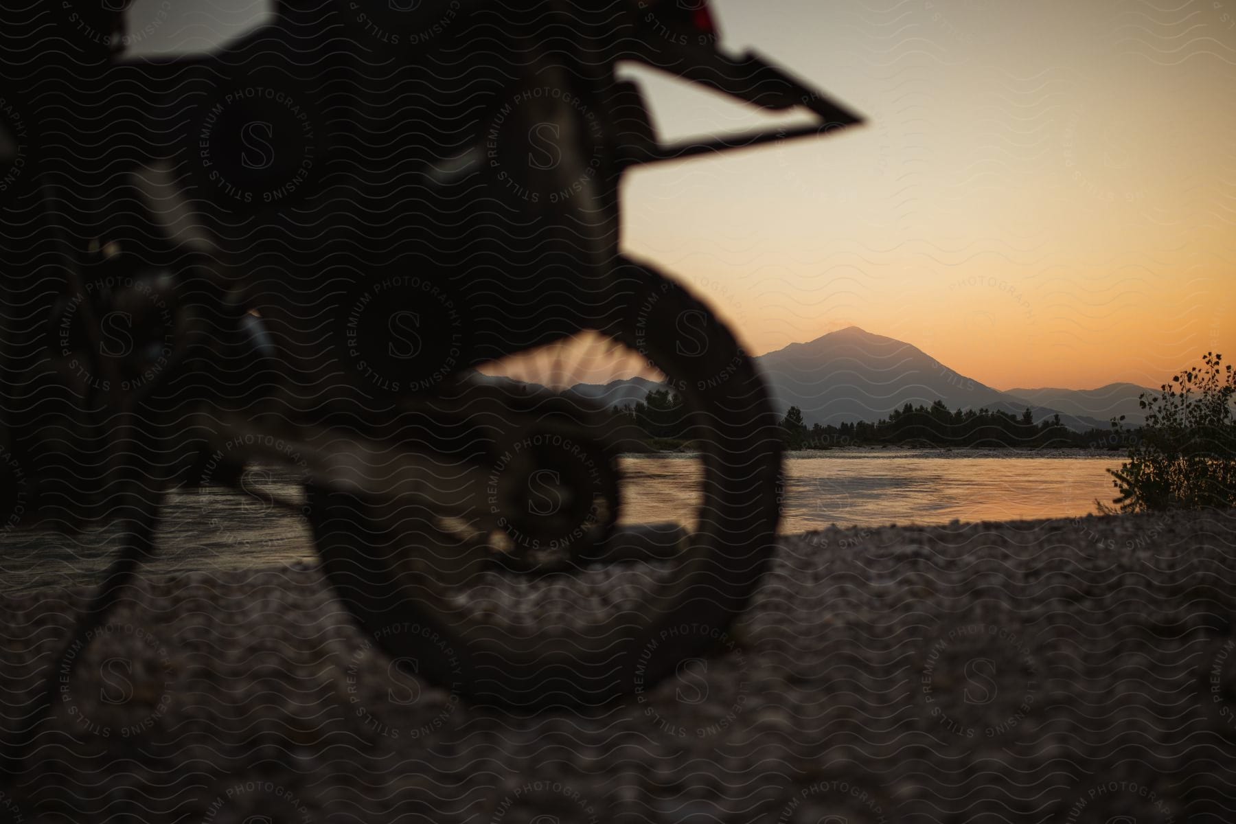 Parked motorcycle next to river with dusk or dawn over mountains in background