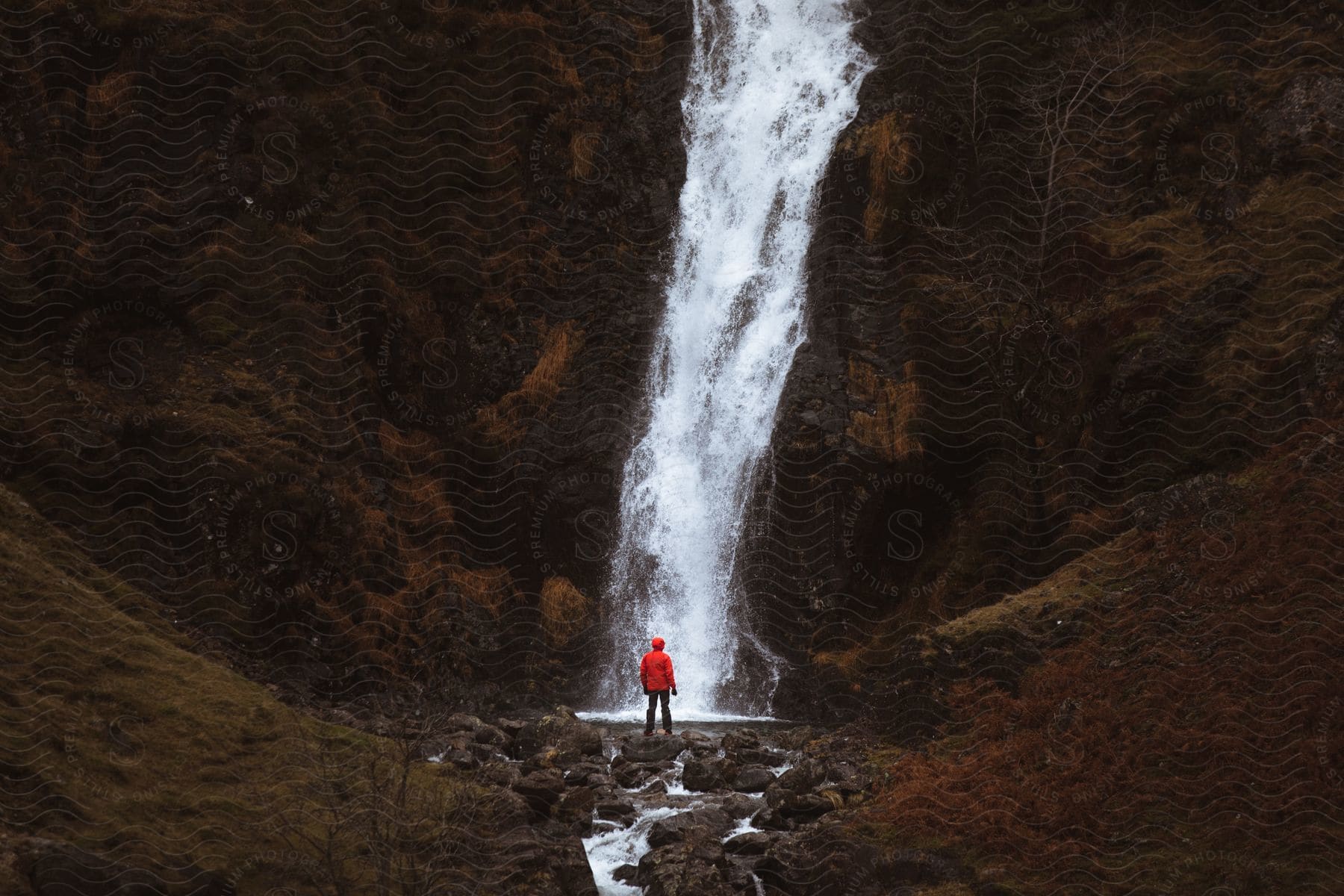 Person in red jacket standing at base of waterfall in the lake district uk