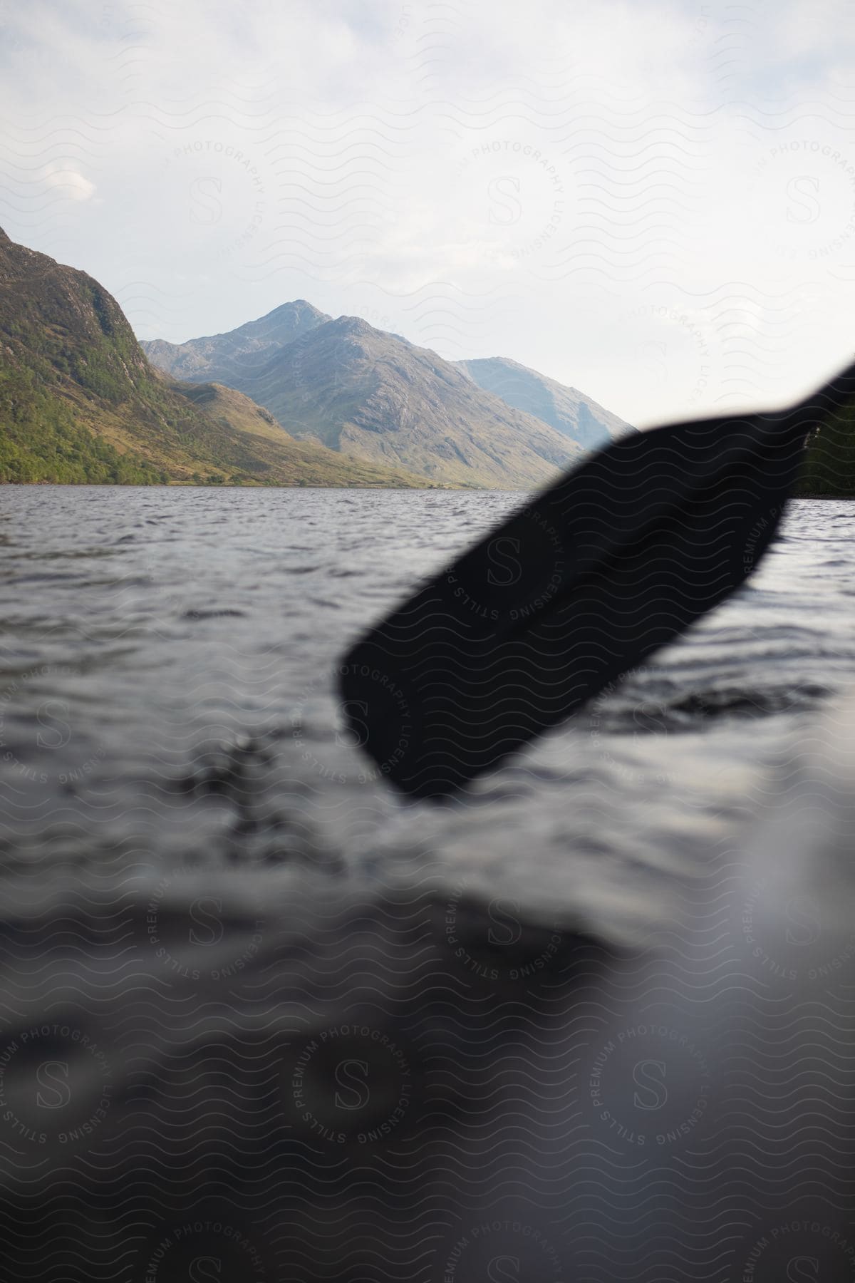 A boat paddle preparing to enter the water of a lake near a mountain range