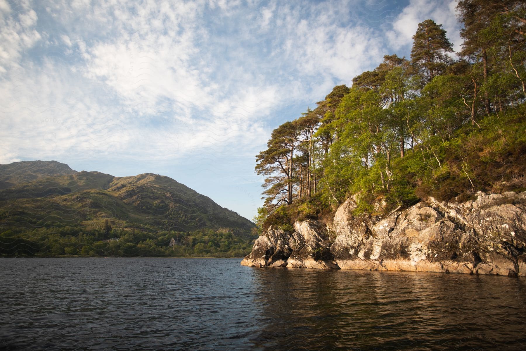 A majestic crag with trees overlooks a serene lake creating a breathtaking landscape