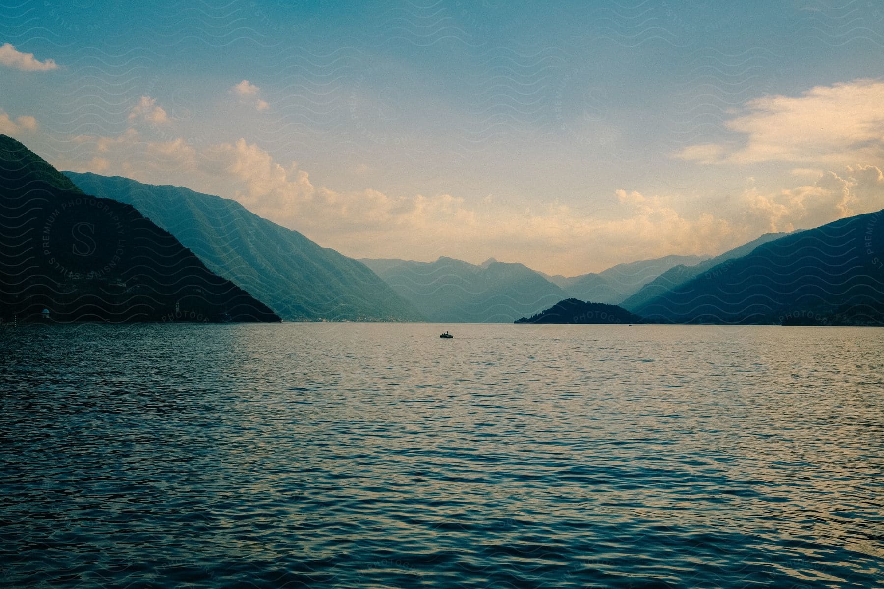 A small boat sails in a river between mountains under a cloudy sky