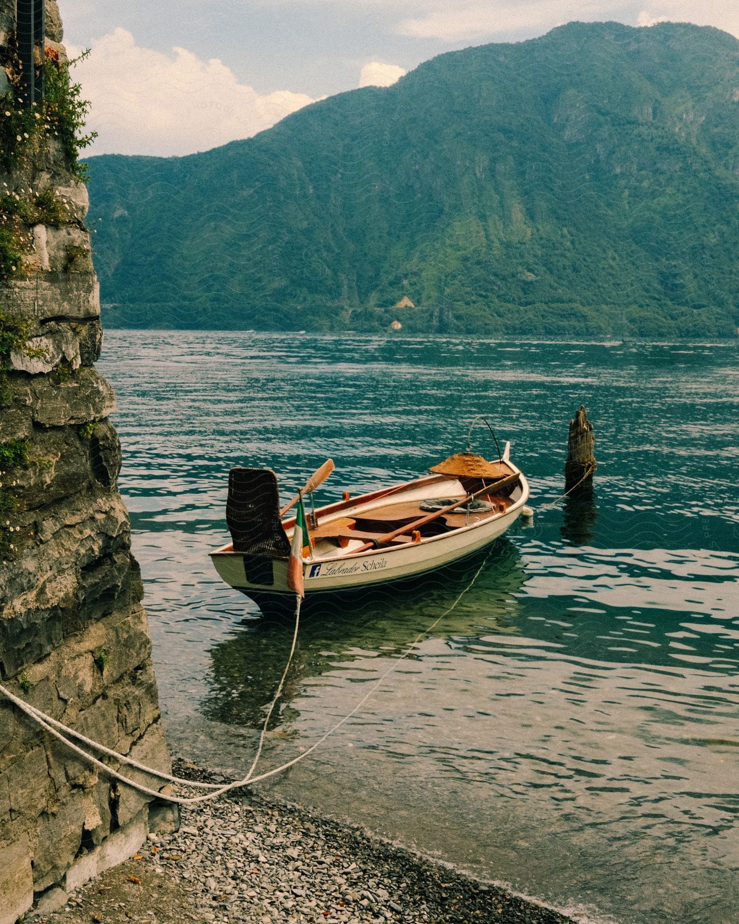 A mountain with green grasses and a river below with a canoe on the water