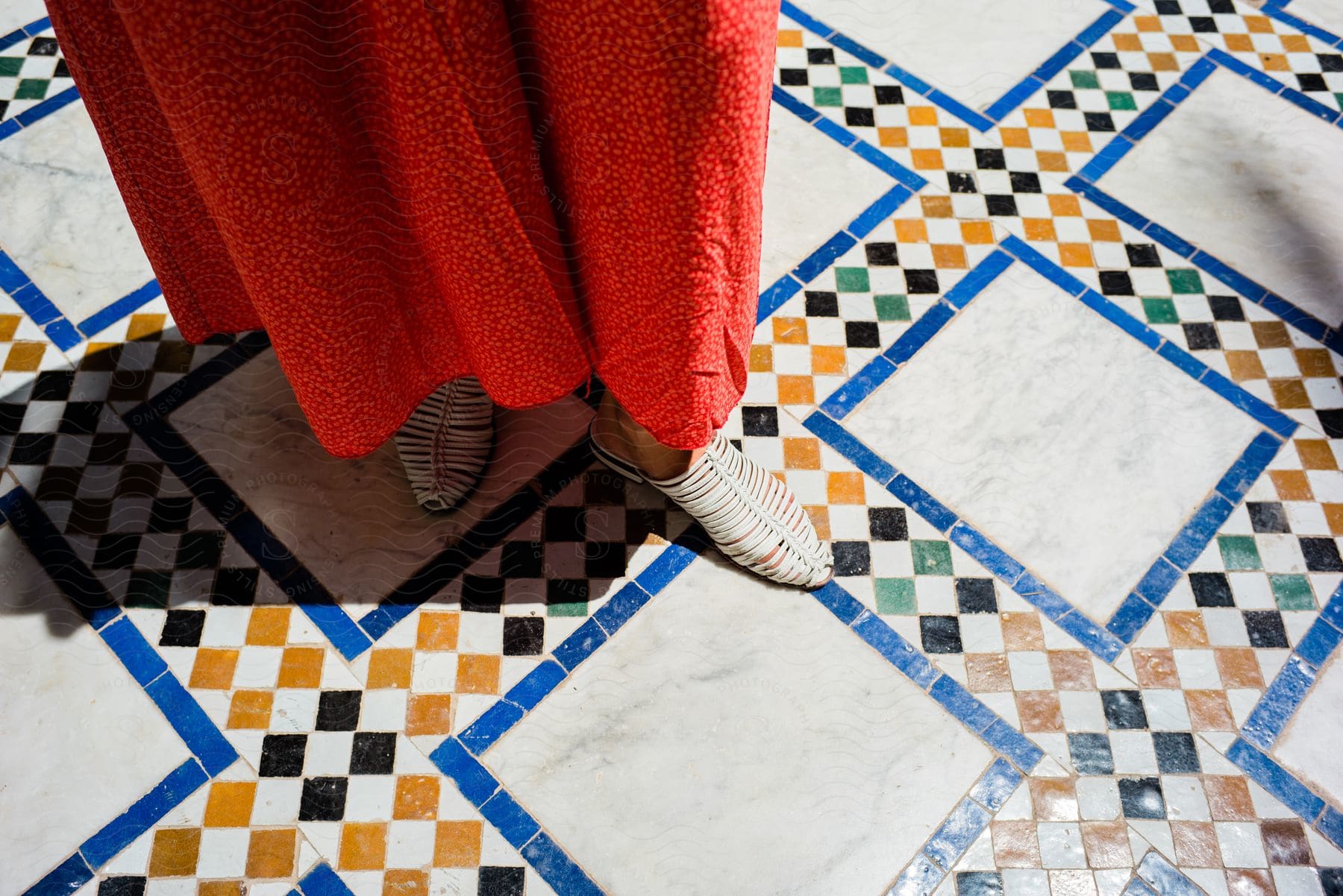A closeup of a womans shoes and dress on a colorful tile floor