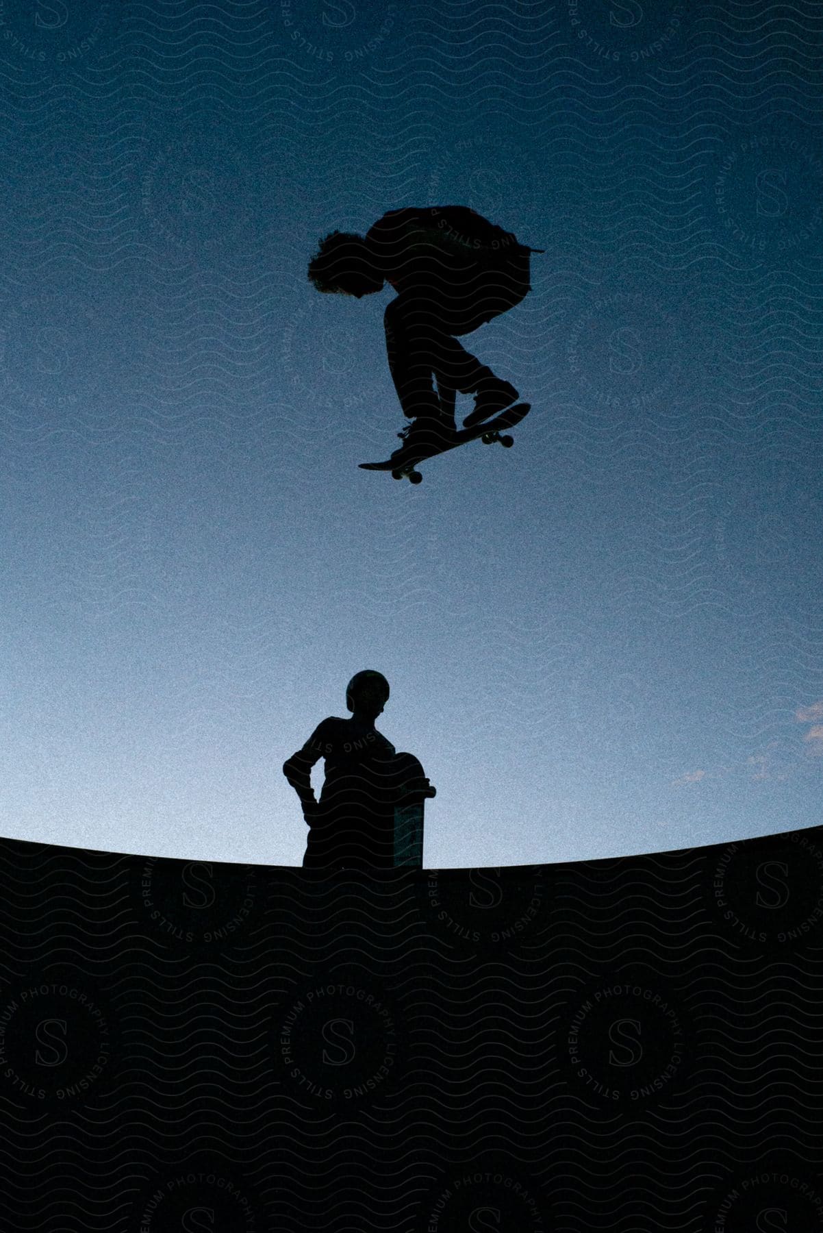 Two human silhouettes doing skateboarding tricks at dusk