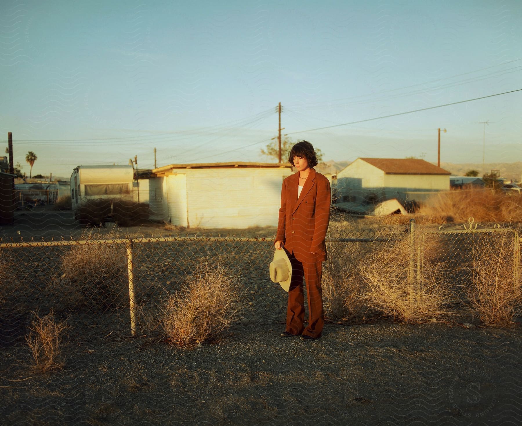 A female poses with a hat in front of a trailer park at dusk