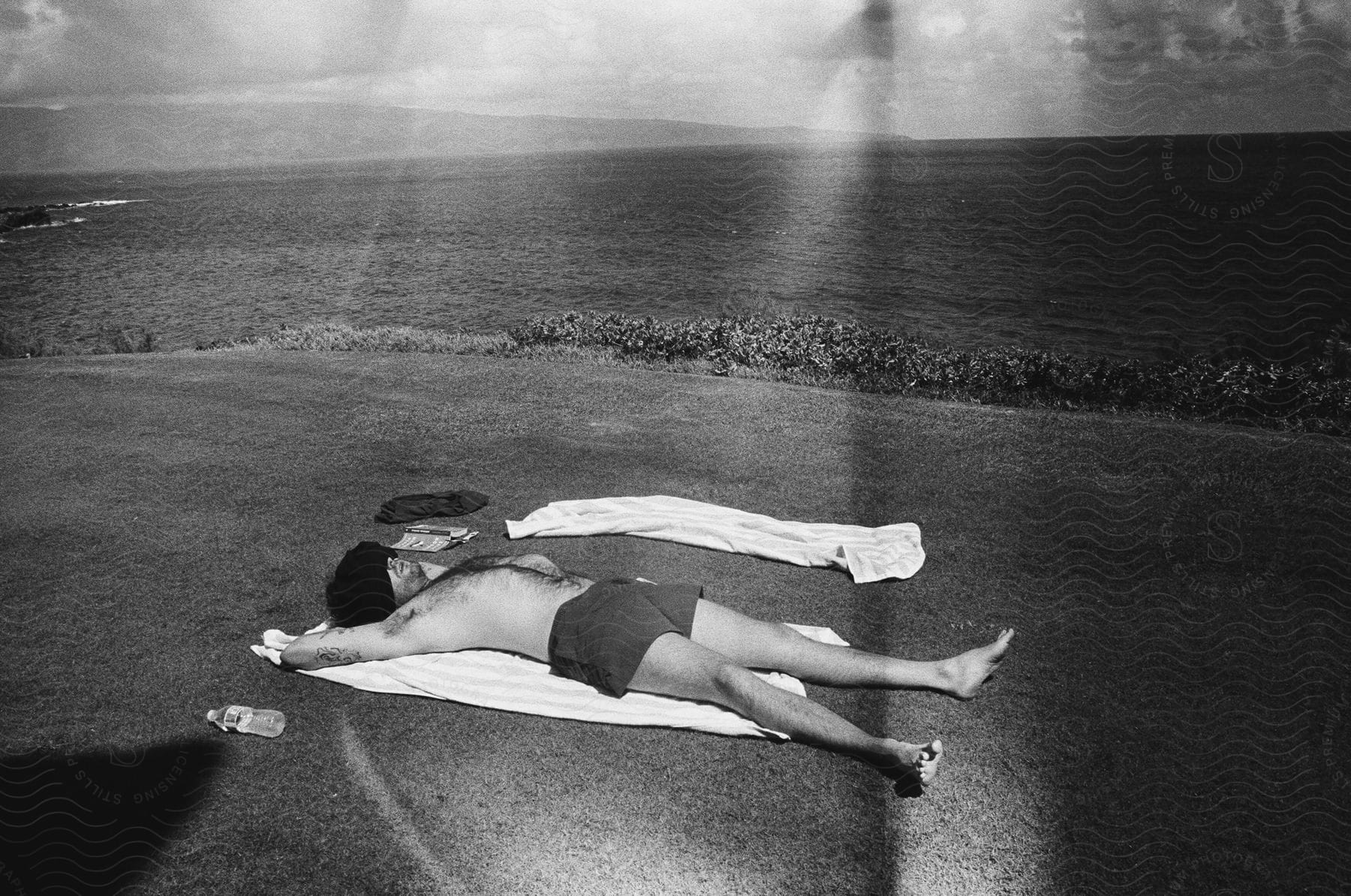 Man lying on a towel on a hill overlooking the ocean wearing swimming shorts