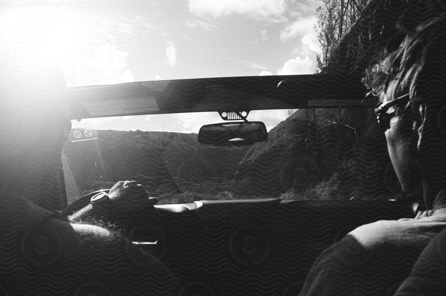 Two people in a car with the sky and clouds in the background wearing sunglasses