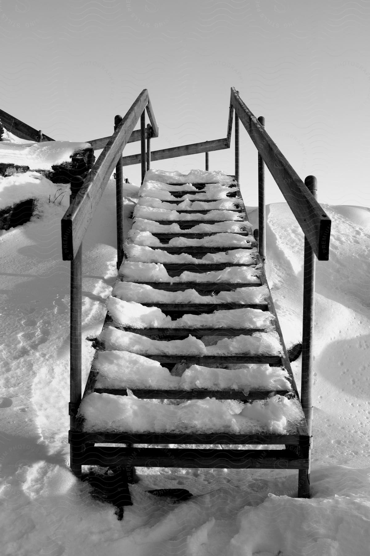 A black and white image of a staircase leading to a house near the water surrounded by snow