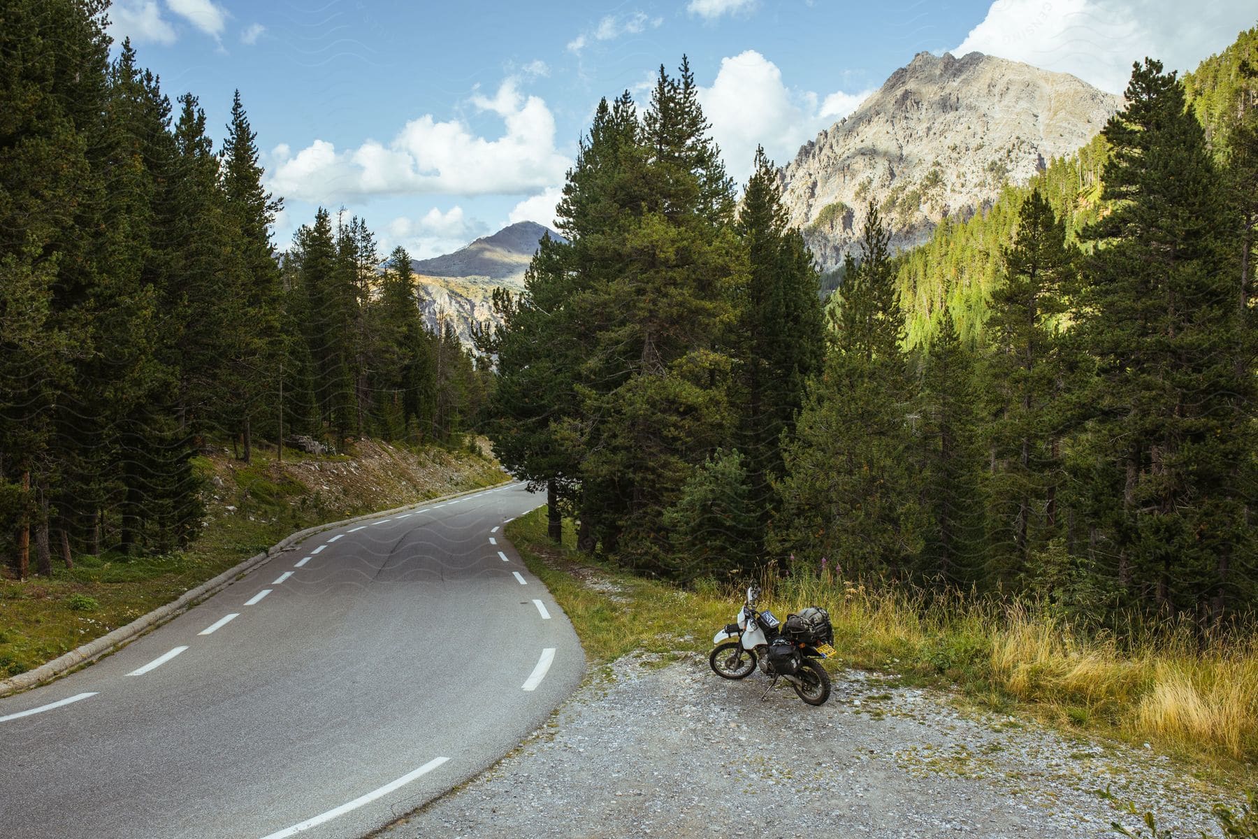 A motorcycle parked on the side of a country road next to trees in the mountains