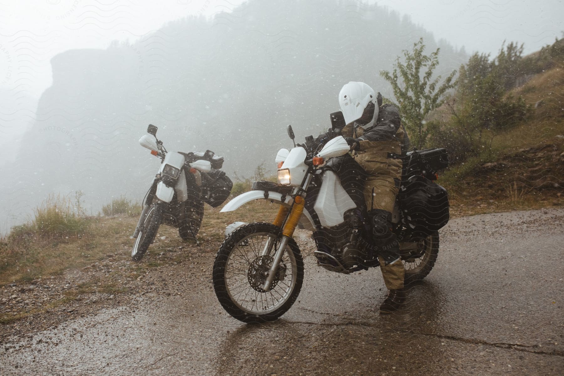 Two motorcycles on the road in a minor snow storm with only one rider on his bike